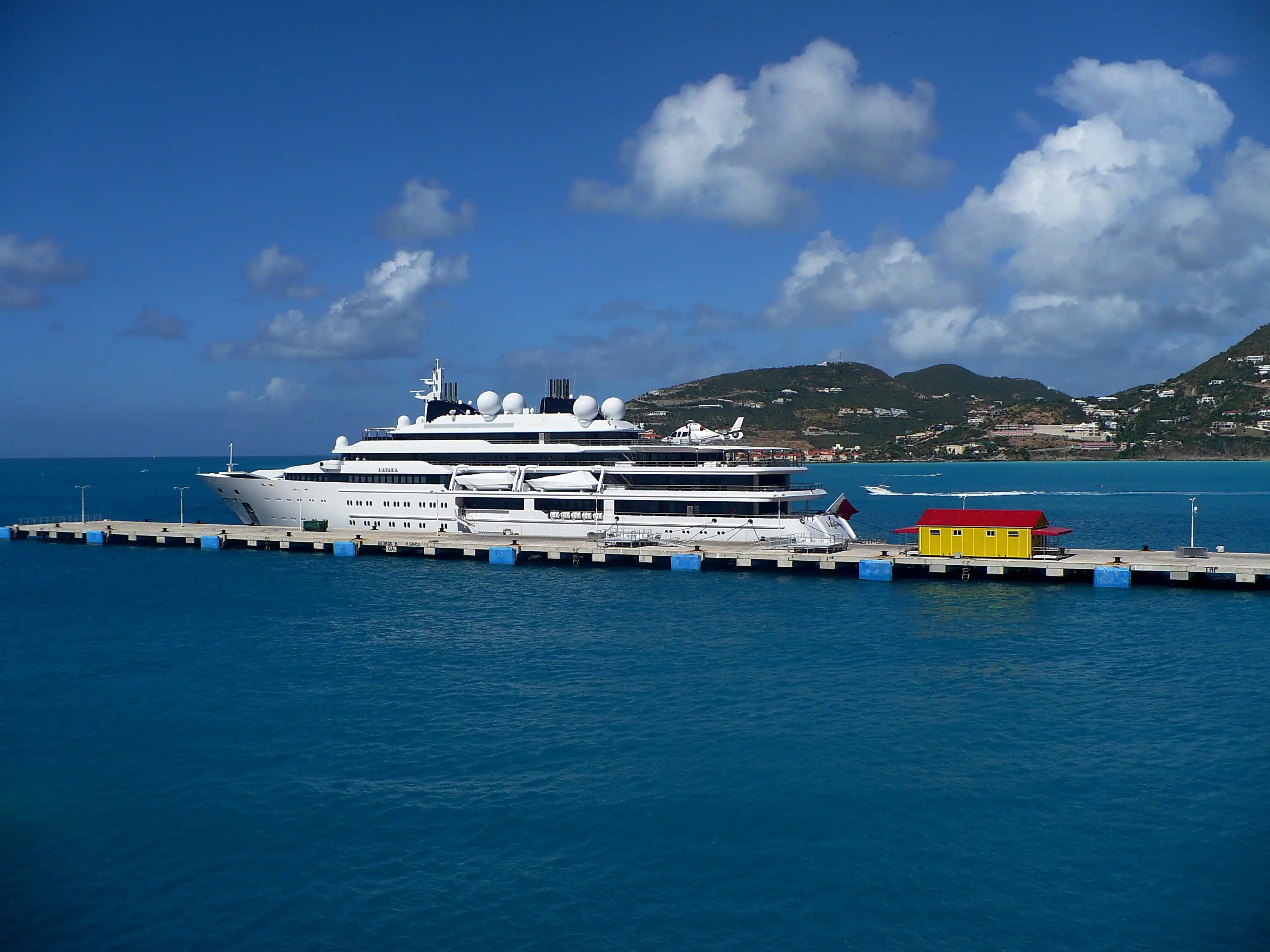 A single white cruise ship berthed alongside the concrete pier at St. Maarten, seen from the shore across calm water