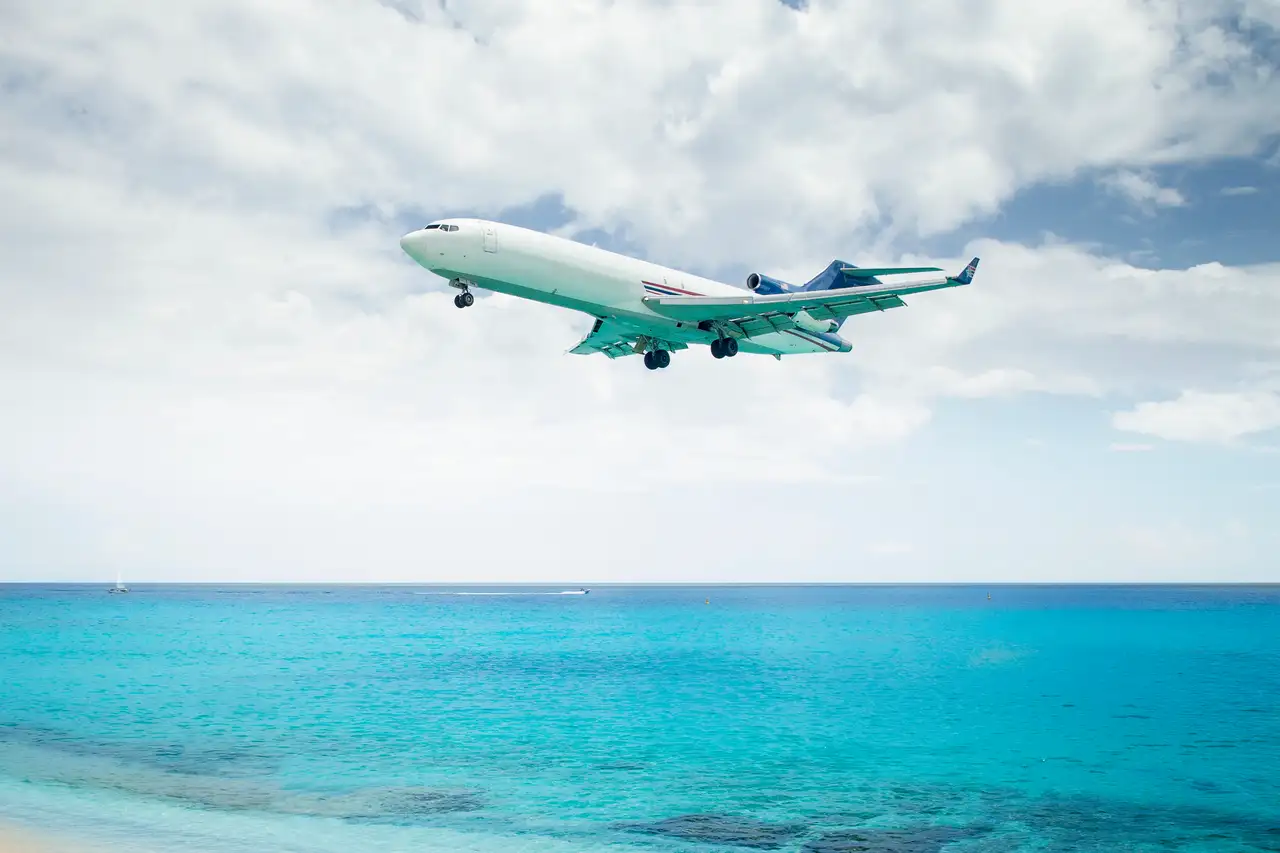 A passenger jet on final approach passing low over the beach and turquoise water at Maho, moments before touchdown