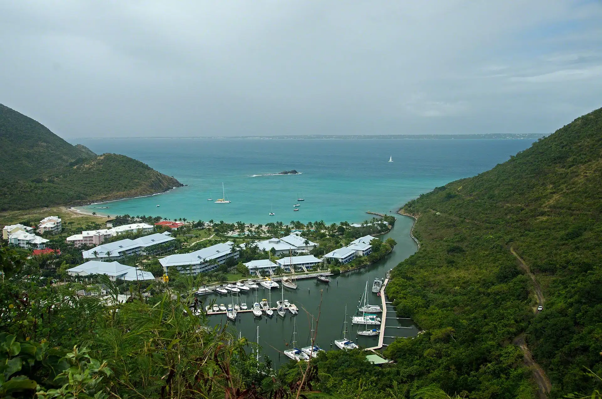 Anse Marcel bay seen from the hillside above, showing the enclosed marina basin behind the beach at the head of the bay