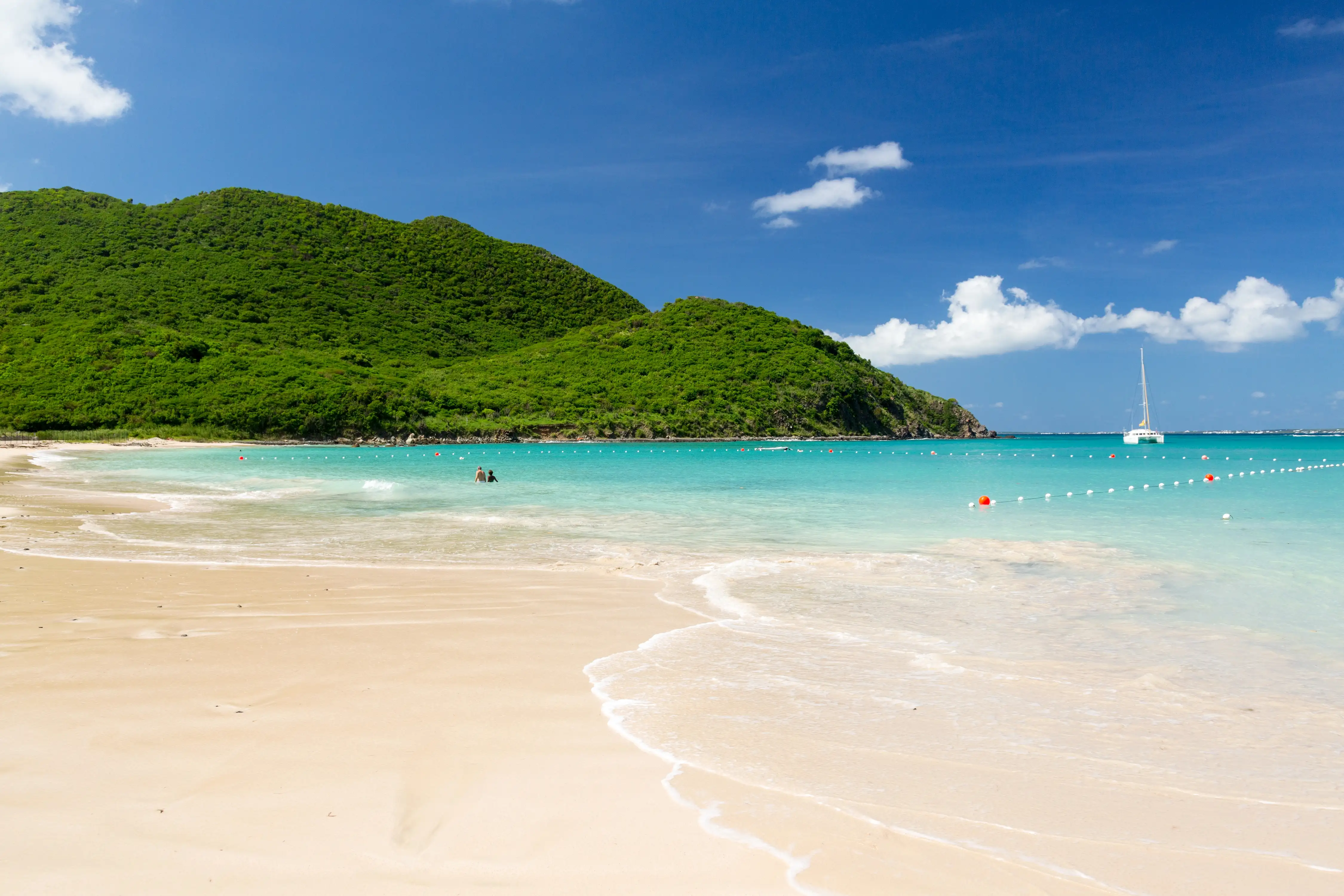 Anse Marcel beach and cove with swimmers in the water and a sailboat anchored near the point