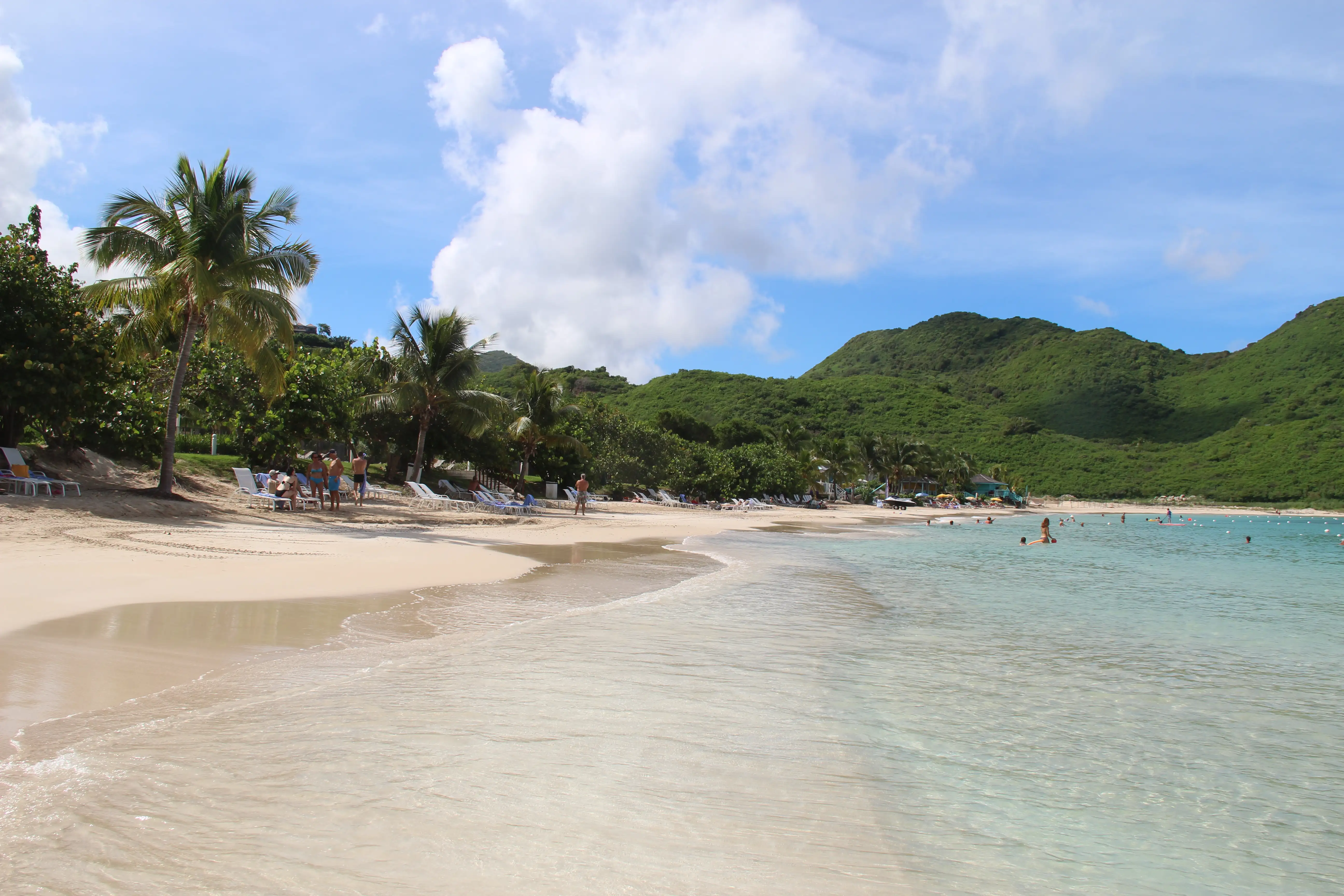 Wide view along Anse Marcel beach with calm shallow water and wooded headlands enclosing the bay on both sides