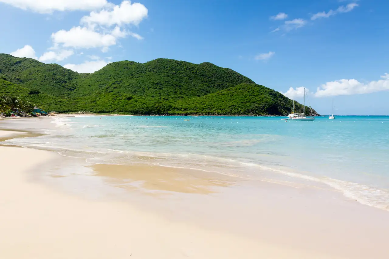 Undeveloped crescent cove at Anse Marcel with hillside greenery and a sailboat anchored offshore