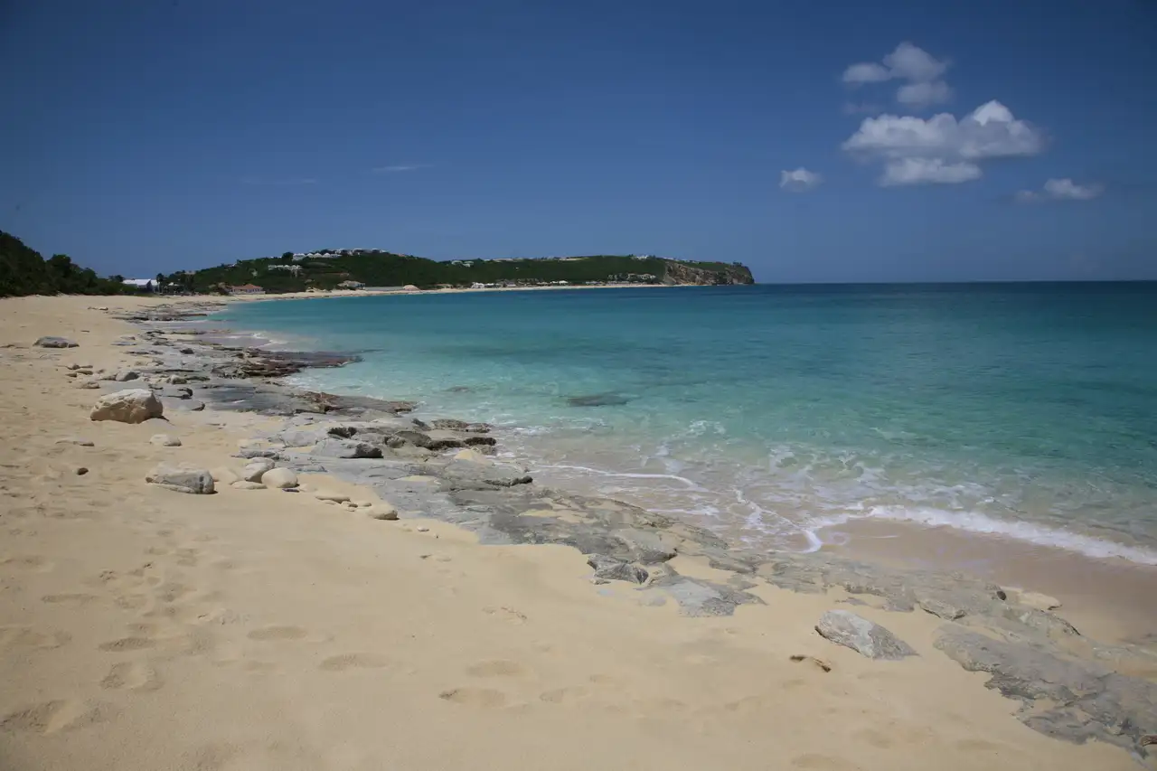 The reddish-gold sand of Baie Rouge running below low ochre cliffs, with clear water along the shoreline