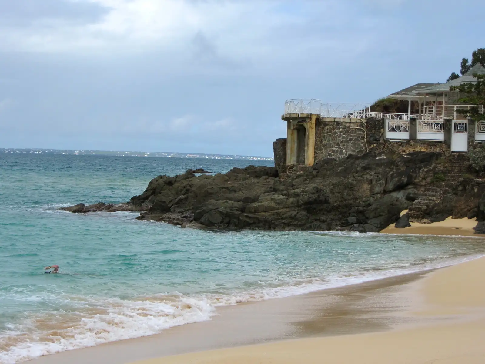 A small second beach at the end of Baie Rouge with dark openings worn into the rock behind it