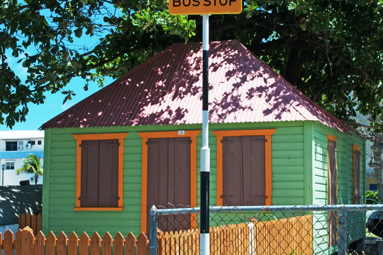 A metal BUS STOP sign on a pole on Front Street in Philipsburg, with parked cars and shopfronts along the street behind it