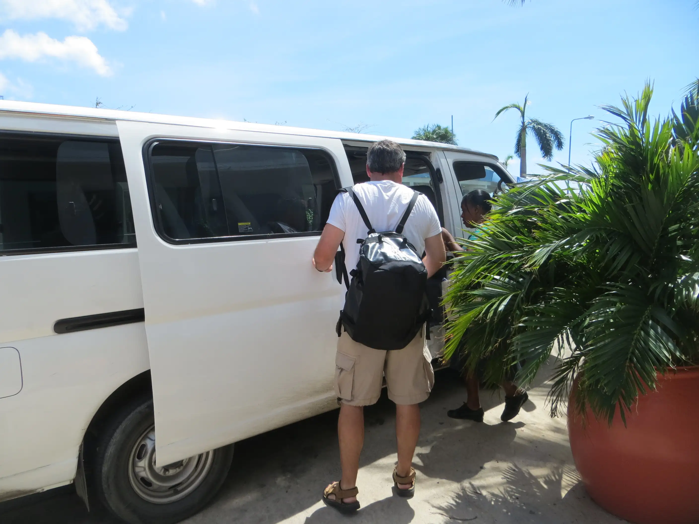 A white passenger minivan pulled over at the roadside with its side door open and a passenger stepping aboard