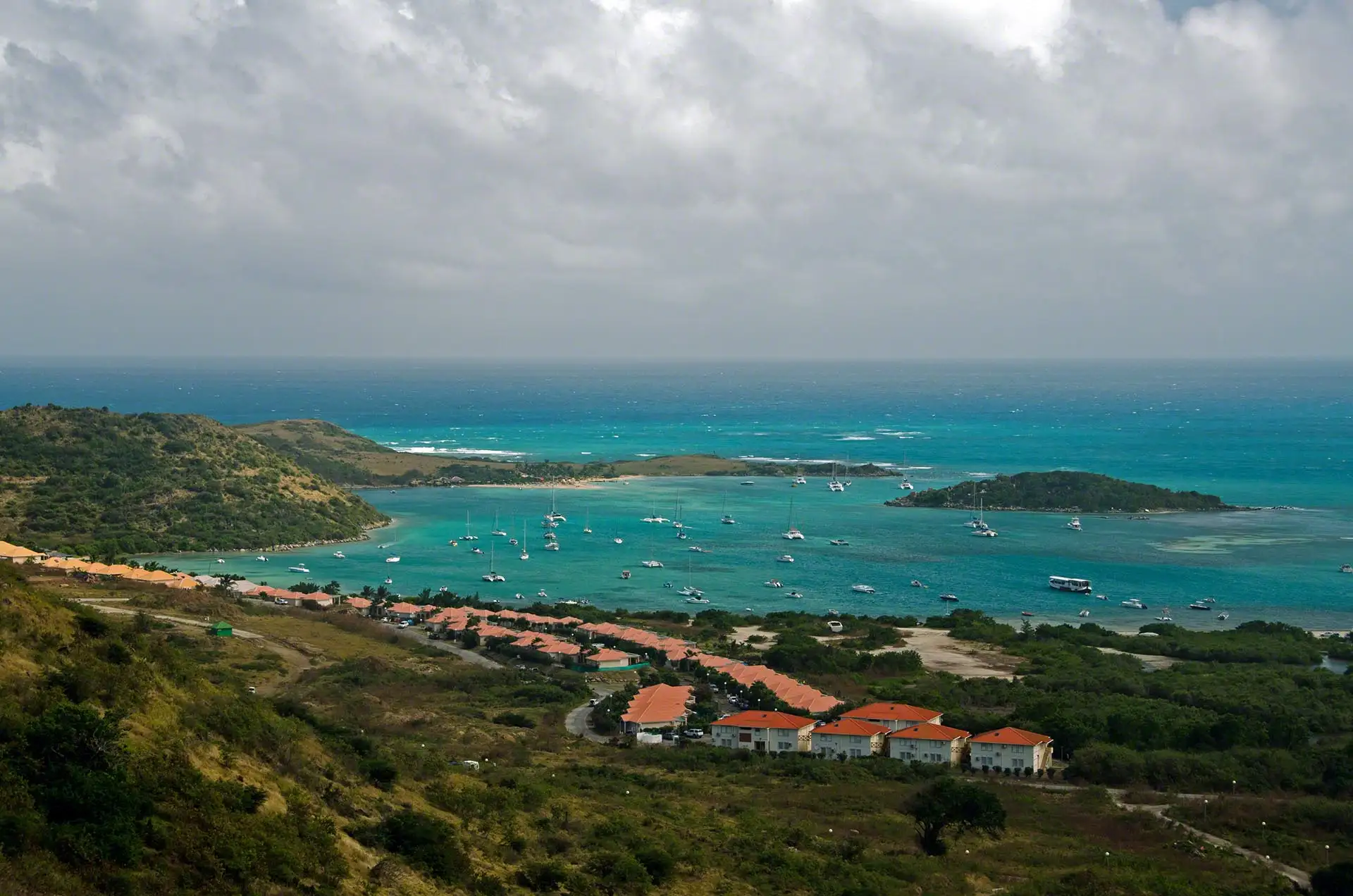Elevated view down over Cul-de-Sac bay, with terracotta-roofed village housing along the shore, yachts anchored in turquoise water and Pinel and a smaller islet lying offshore
