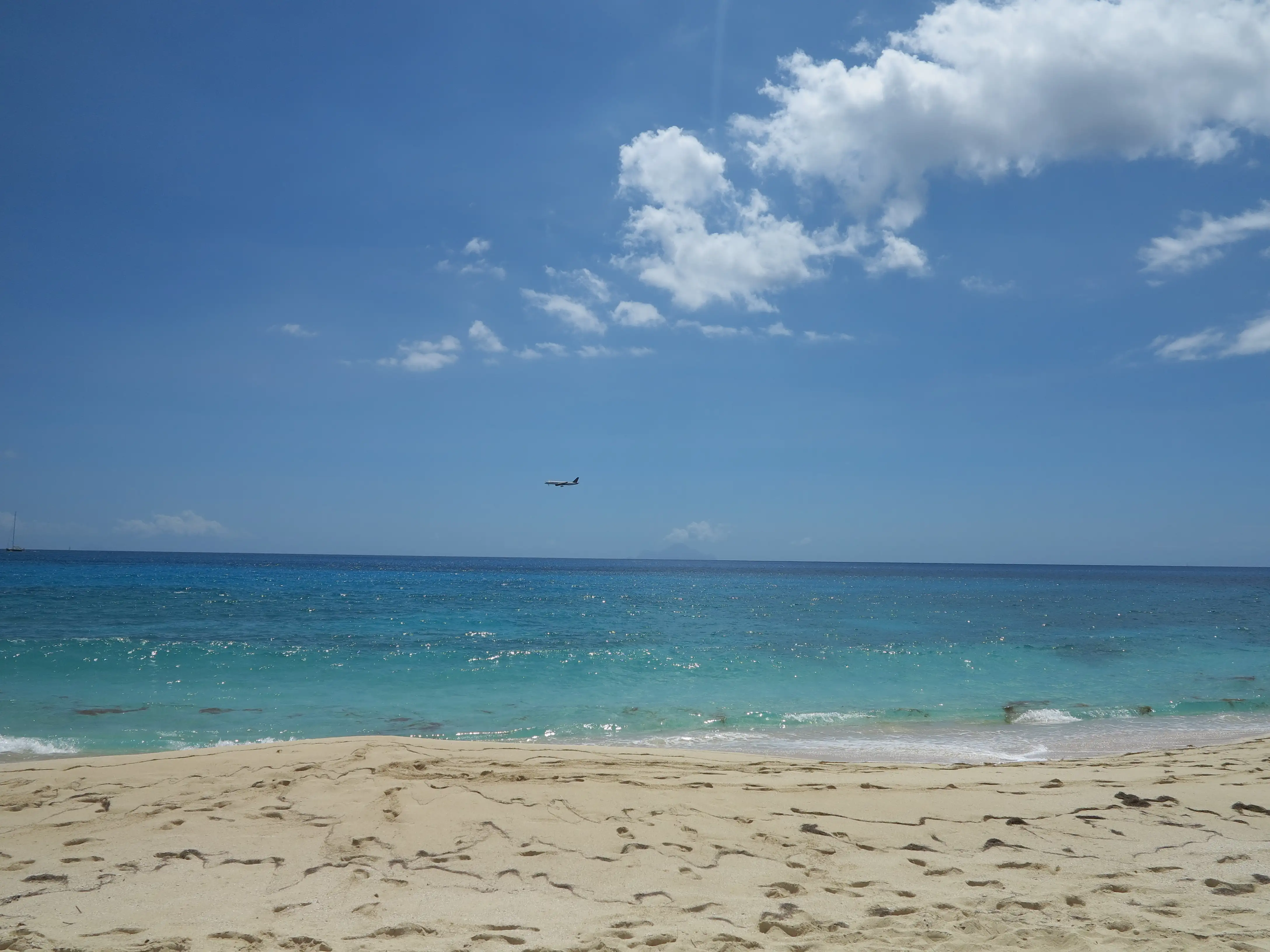 Empty sandy beach at Cupecoy with footprints in the sand and the island of Saba visible on the horizon