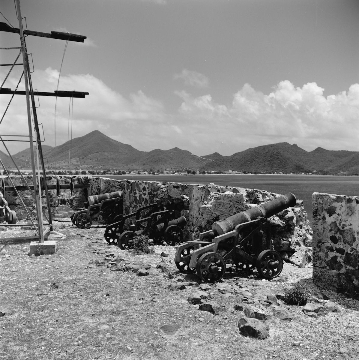A grassy bastion of a ruined fort on a headland, with the roofs of Philipsburg and a wide bay visible beyond.