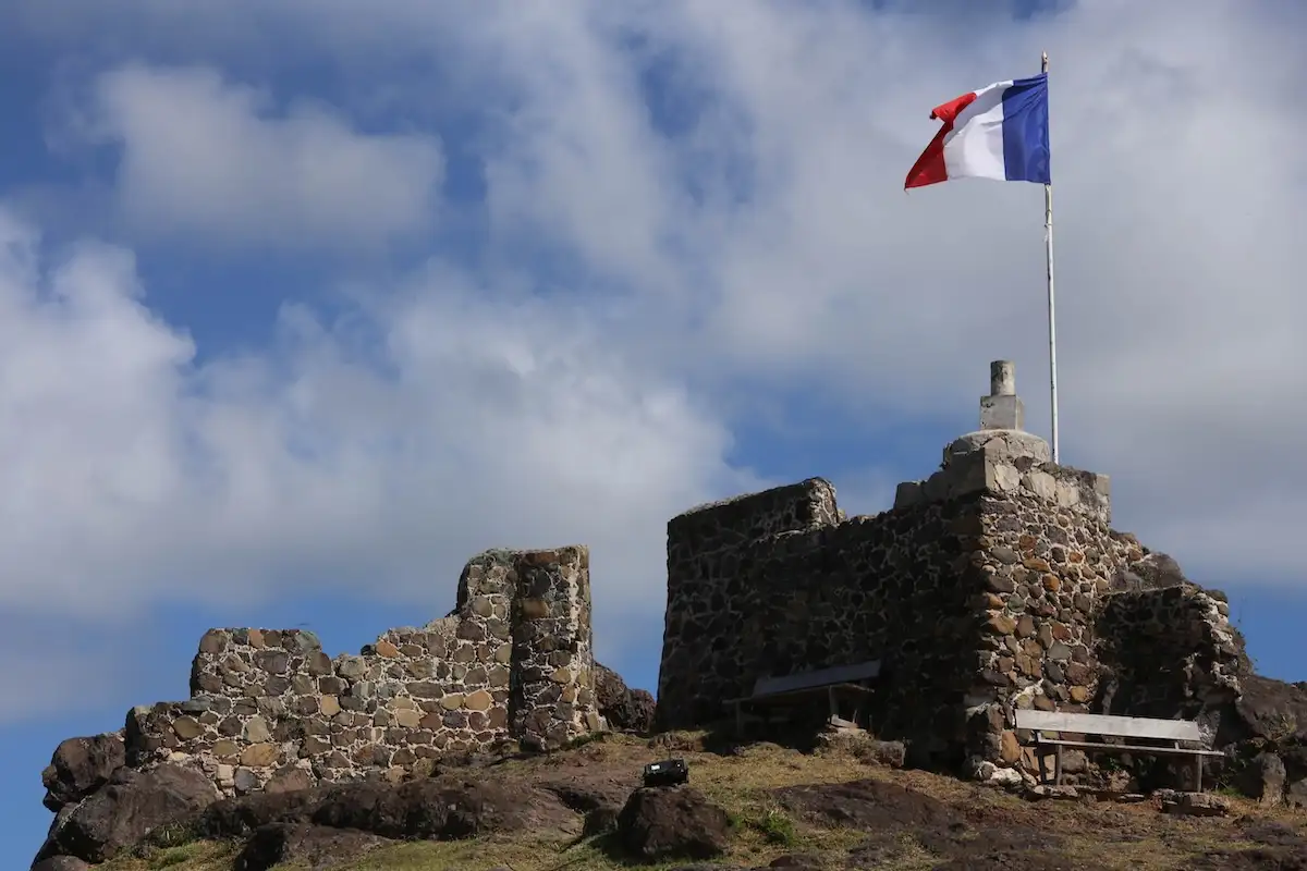 The stone ruins of a hilltop fort with a French flag flying from a pole, overlooking Marigot bay and the sea beyond
