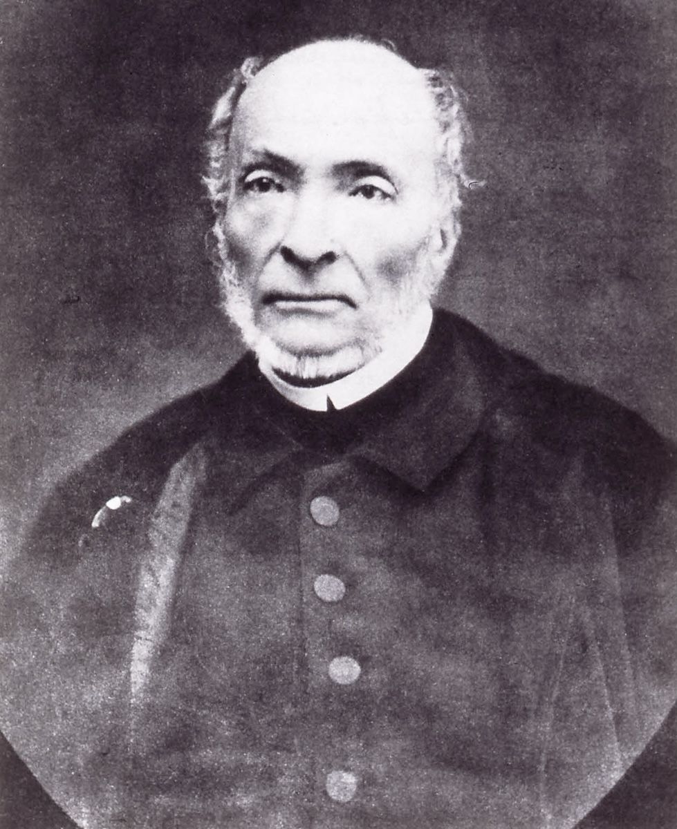 A grainy photographic portrait of an elderly man with white side whiskers in a dark buttoned coat.