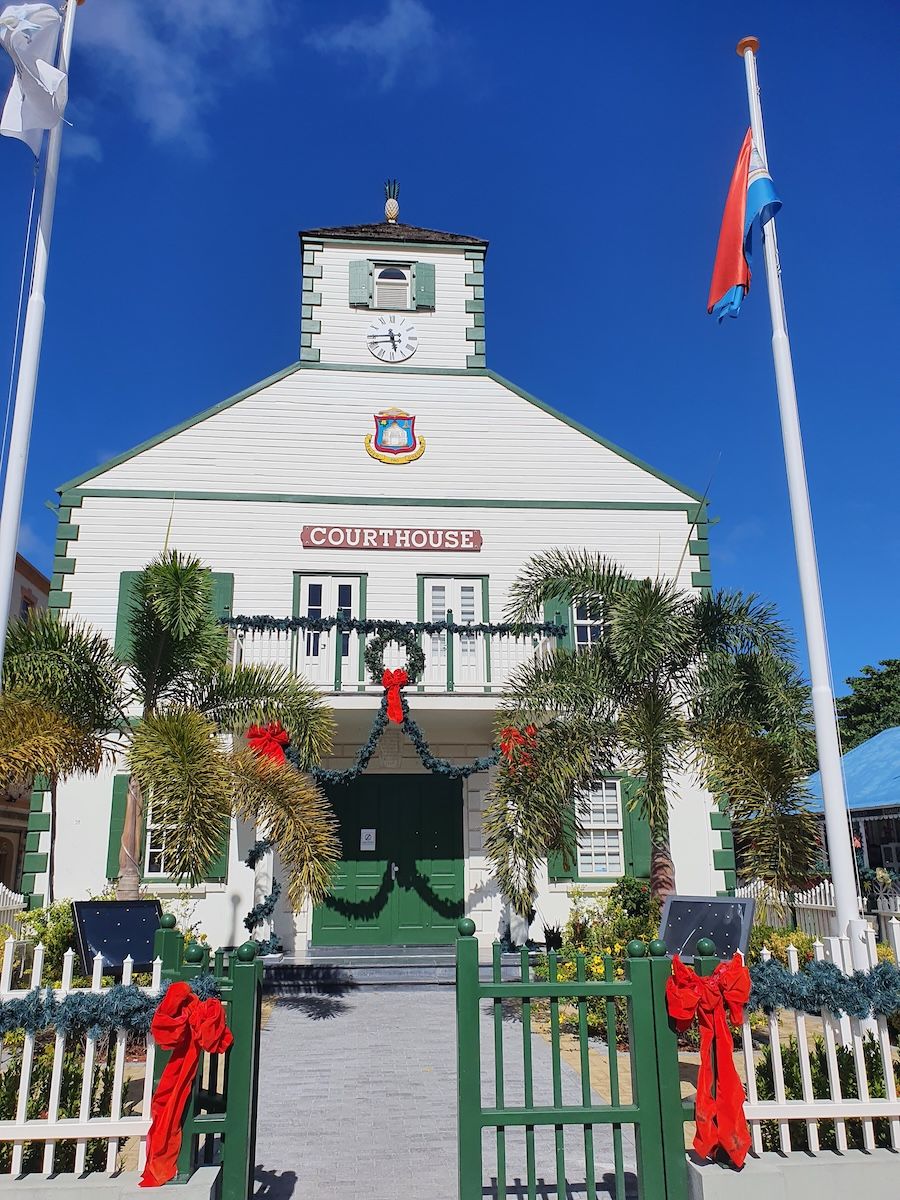 The white and green Philipsburg Courthouse with its clock tower and pineapple finial, the Sint Maarten coat of arms on its gable, decorated with Christmas garlands and flying the Sint Maarten flag.