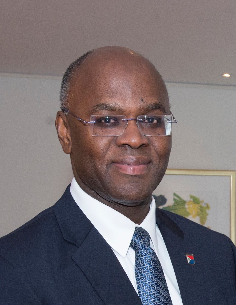A portrait of Eugene Holiday in a dark suit and blue tie, wearing a Sint Maarten flag lapel pin.