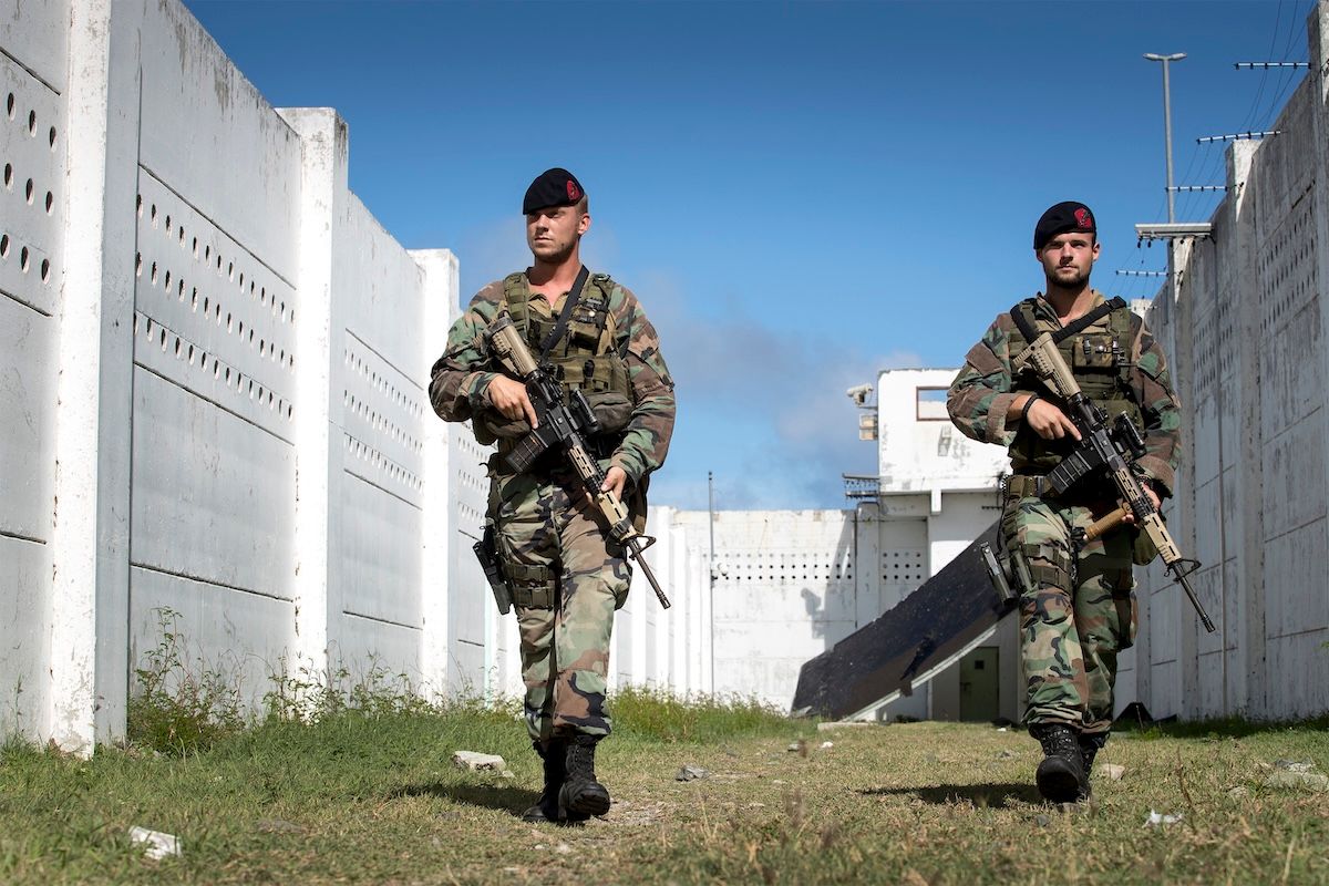 Two Dutch marines in camouflage carrying rifles walk between damaged concrete walls during the relief operation after Hurricane Irma.