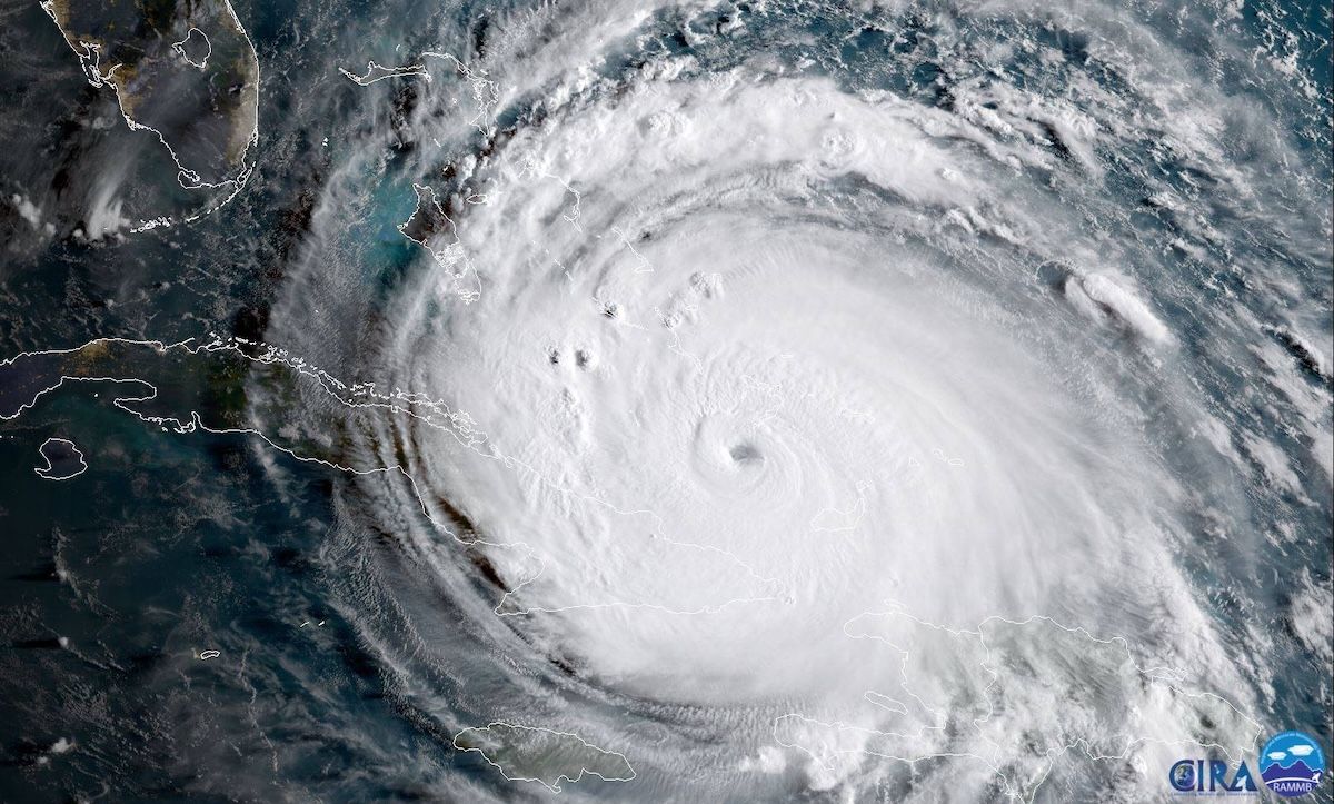 A satellite view of Hurricane Irma as a vast white spiral with a clear eye, filling the sea between Cuba and the Bahamas with Florida at the upper left.