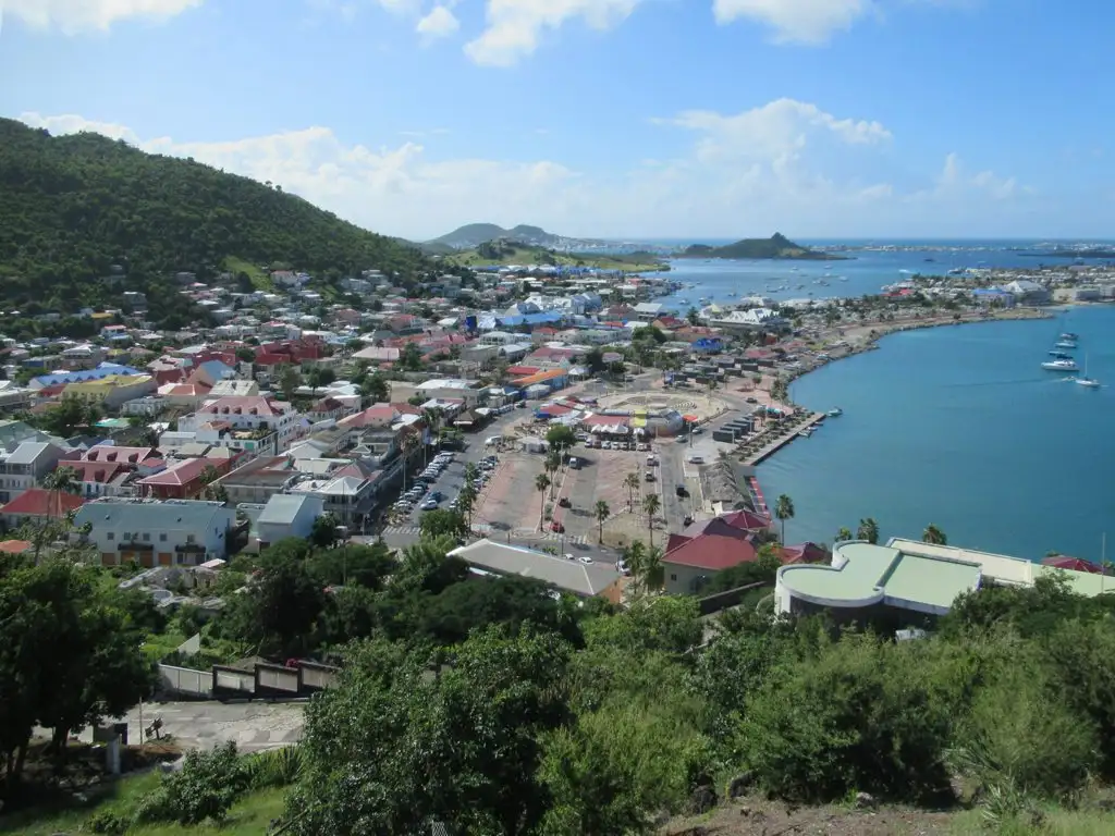 A view from the hill at Fort Louis over the red and pastel rooftops of Marigot, its waterfront square and marina, with boats moored in the bay