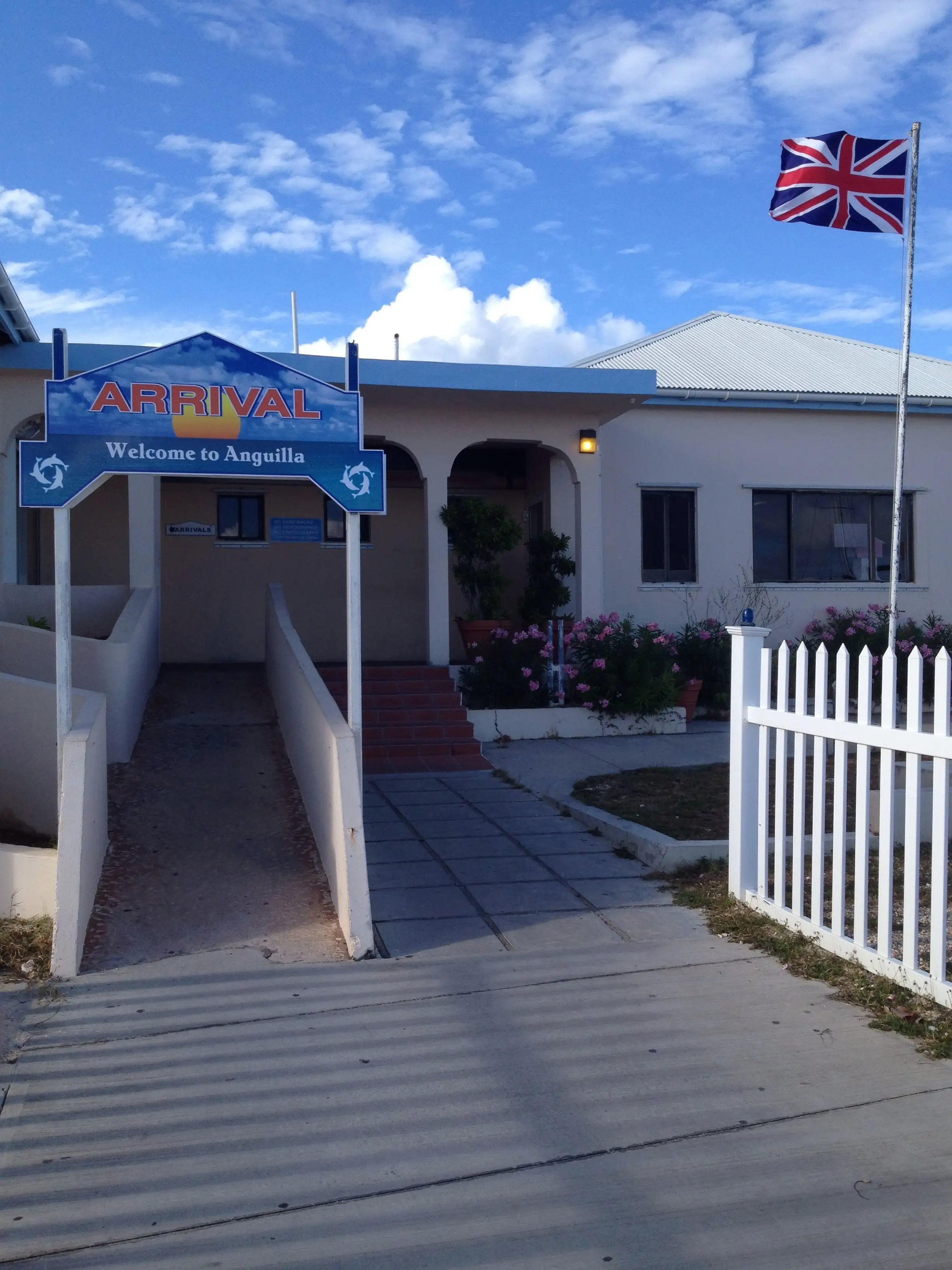 A low white building at Blowing Point signed ARRIVAL and Welcome to Anguilla, with a Union Jack flying above the entrance