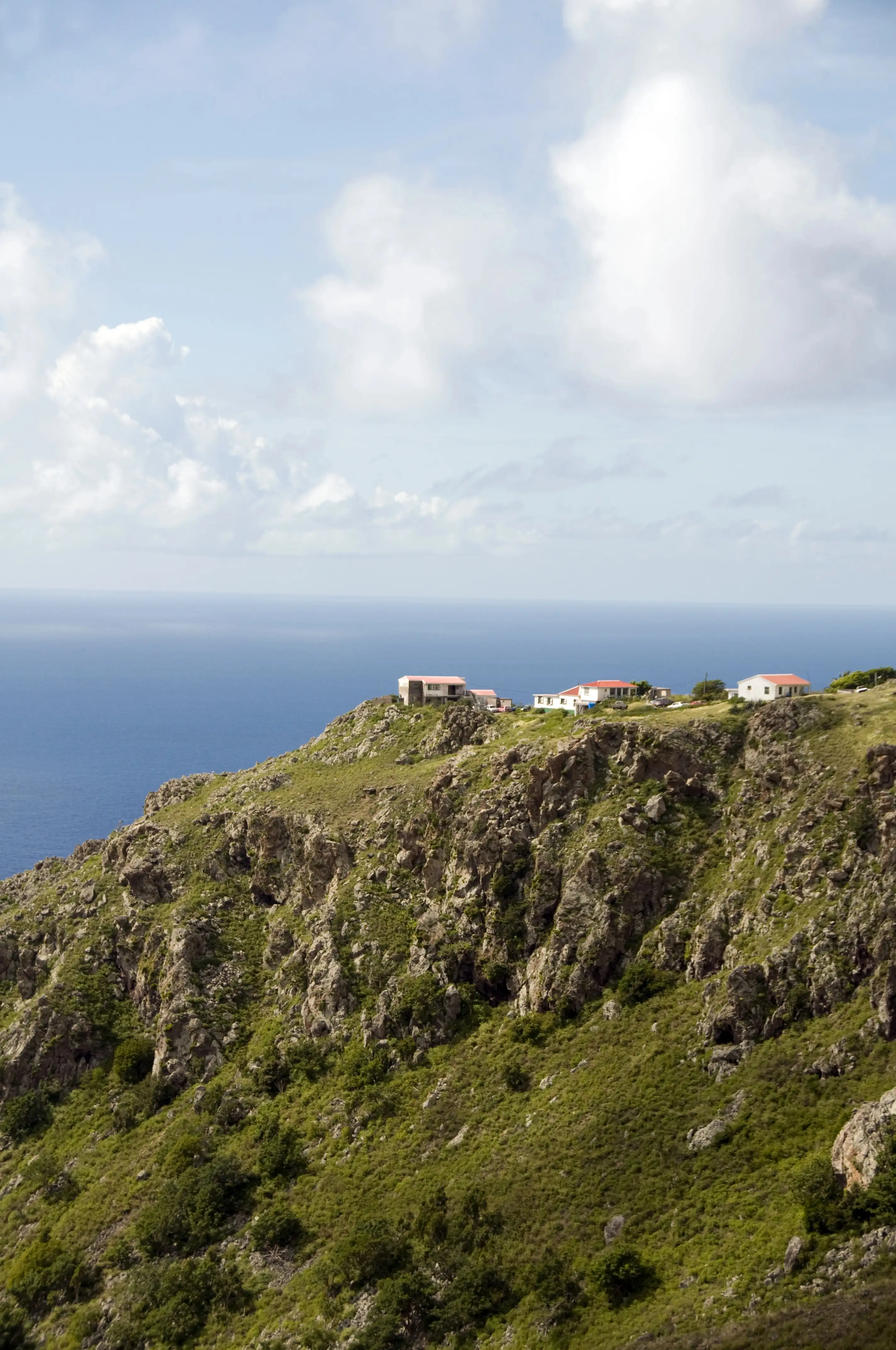 White houses with red roofs perched on a steep green mountainside above the Caribbean Sea on Saba