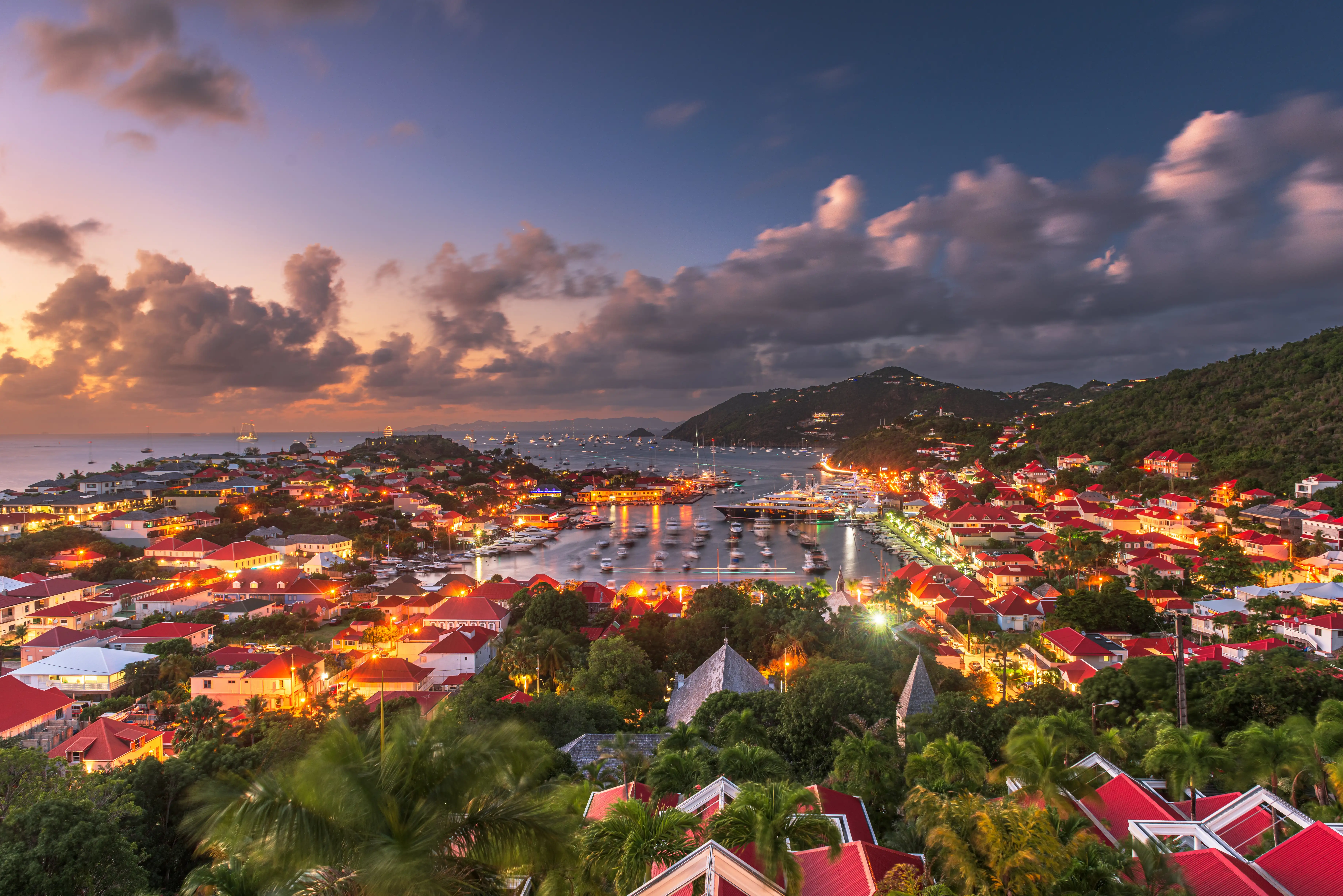 Gustavia harbour at dusk, the town lights coming on along the waterfront and yachts silhouetted against a fading sky