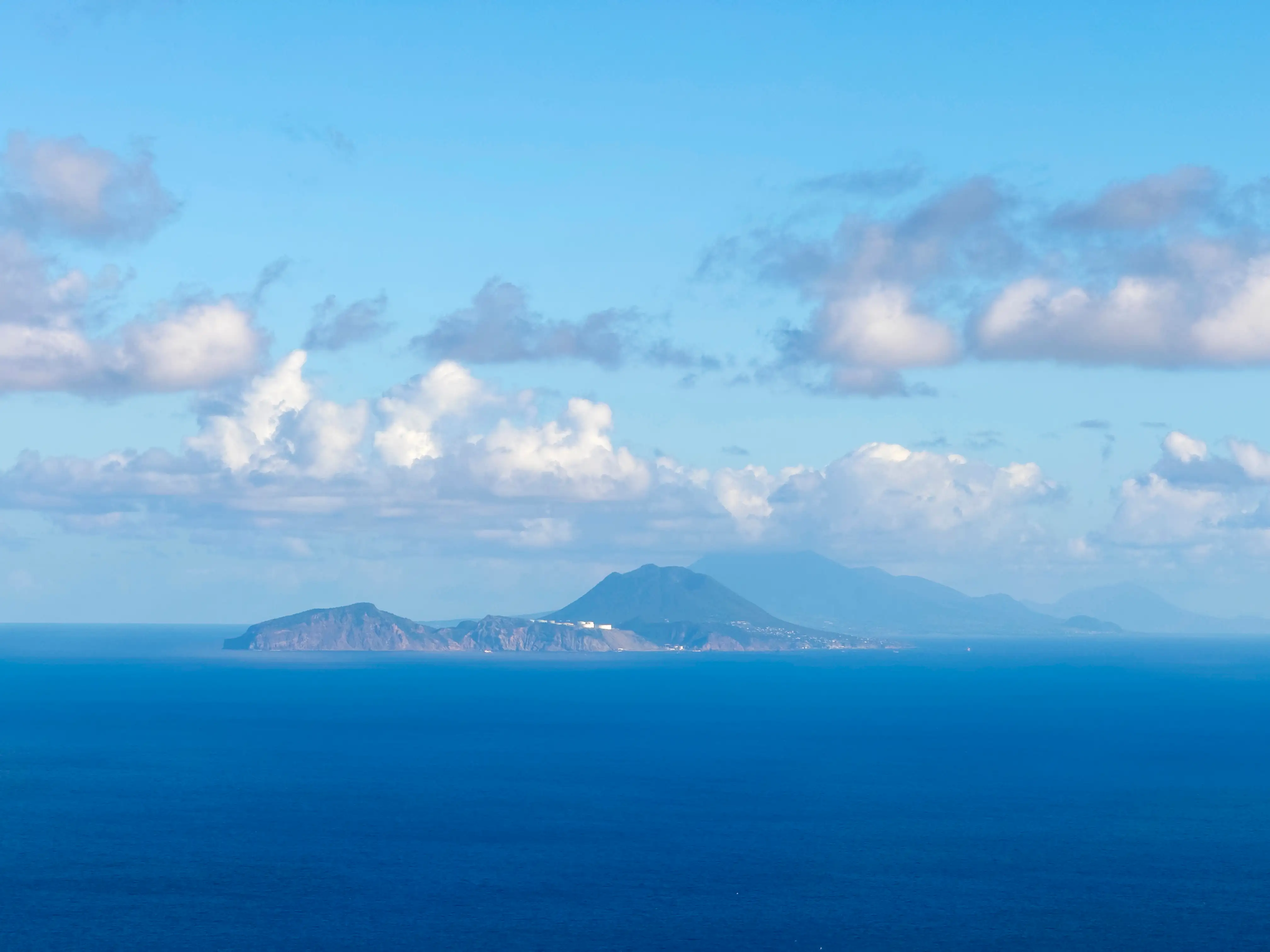 The island of Sint Eustatius seen at a distance across open water, the cone of The Quill rising at one end and St. Kitts faint on the horizon behind