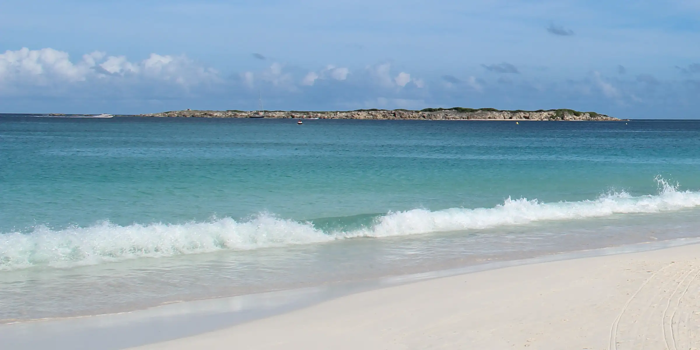 The low green islet of Caye Verte sitting offshore in turquoise water, seen from the Orient Bay shoreline