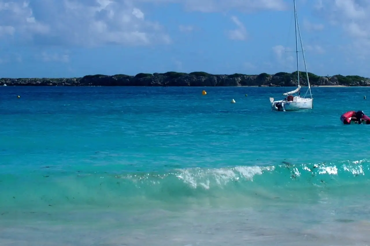 The low green islet of Caye Verte sitting on the horizon in turquoise water off Orient Bay