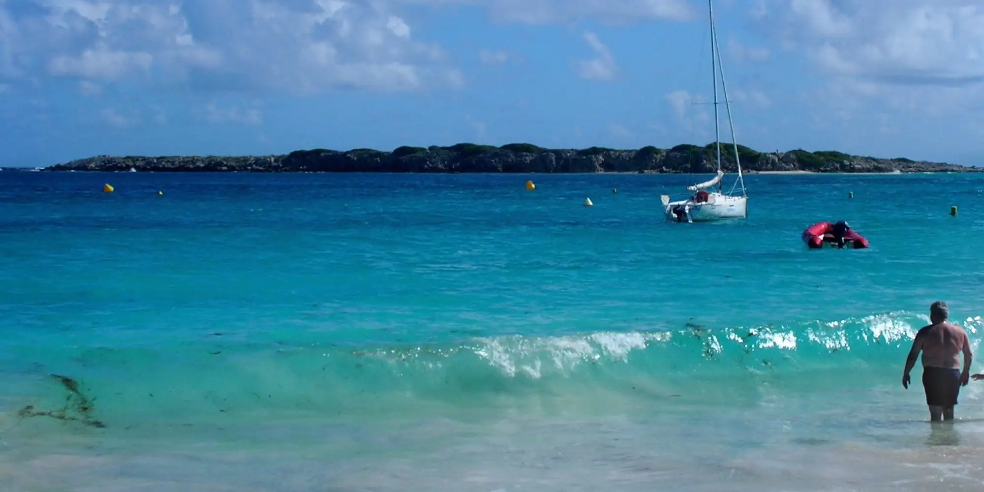 The low green islet of Caye Verte sitting on the horizon in turquoise water off Orient Bay