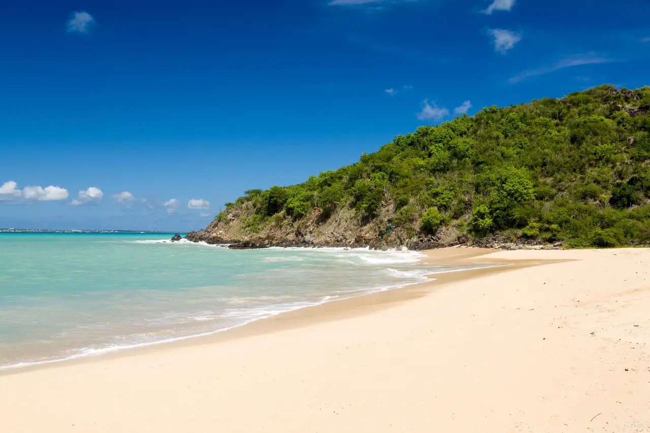 Empty crescent of white sand at Happy Bay, St. Martin, with turquoise water and a green, undeveloped headland
