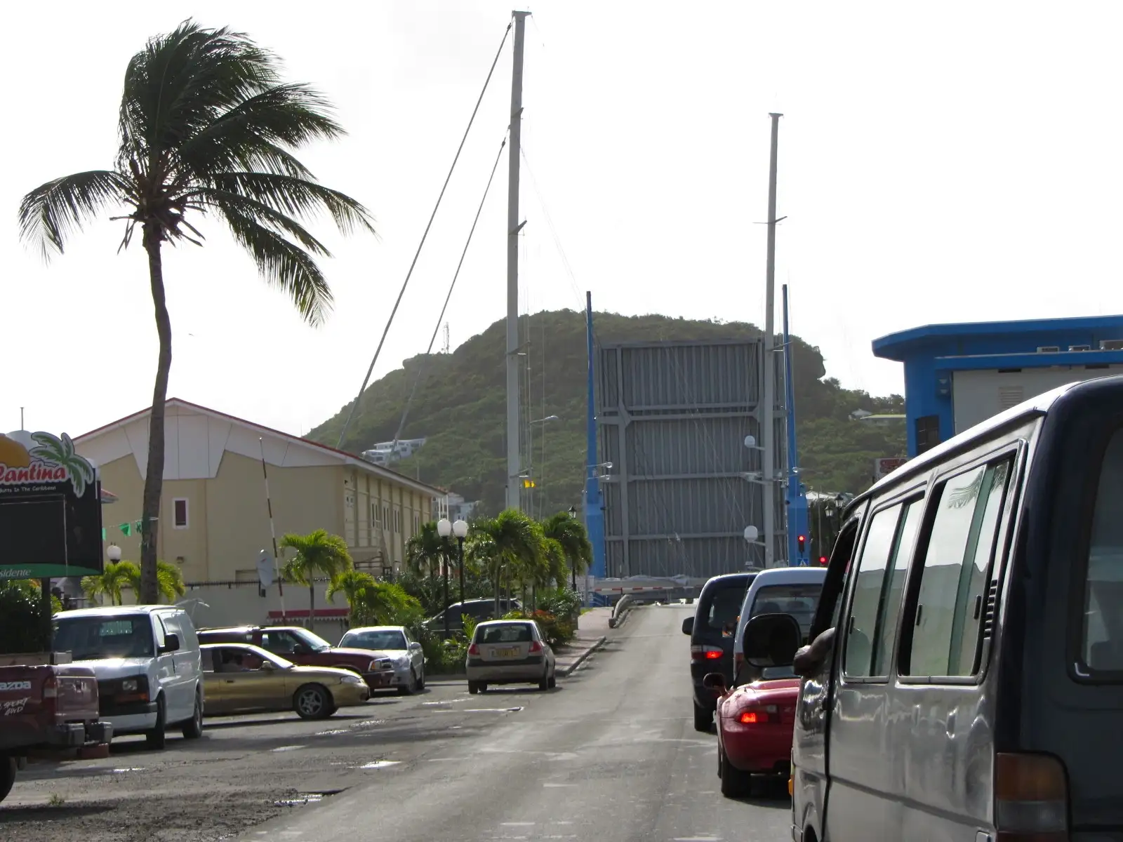 The Simpson Bay lift bridge raised with its roadway tilted upward, a sailing mast passing through, and cars queued on the approach