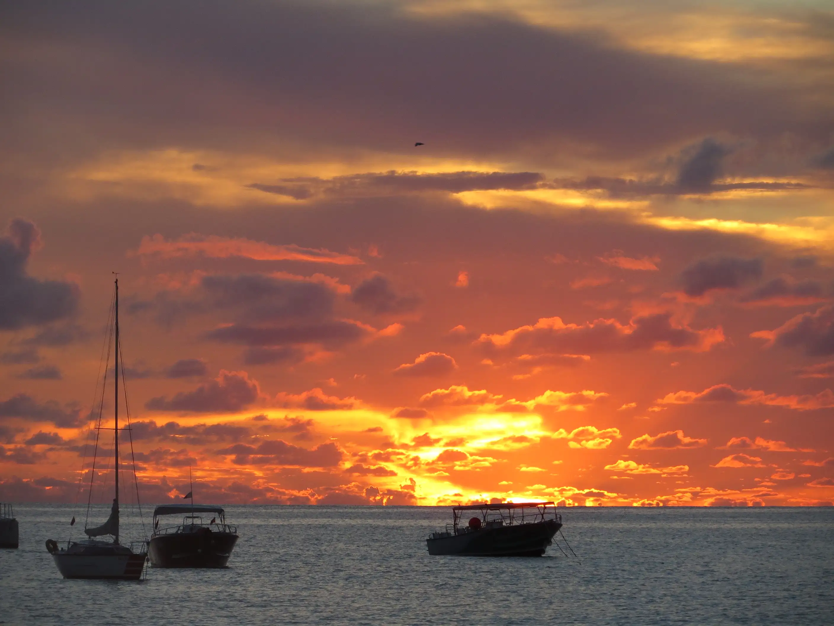 The sun setting over the water off Kim Sha Beach in Simpson Bay, the sky and sea lit orange behind a dark shoreline