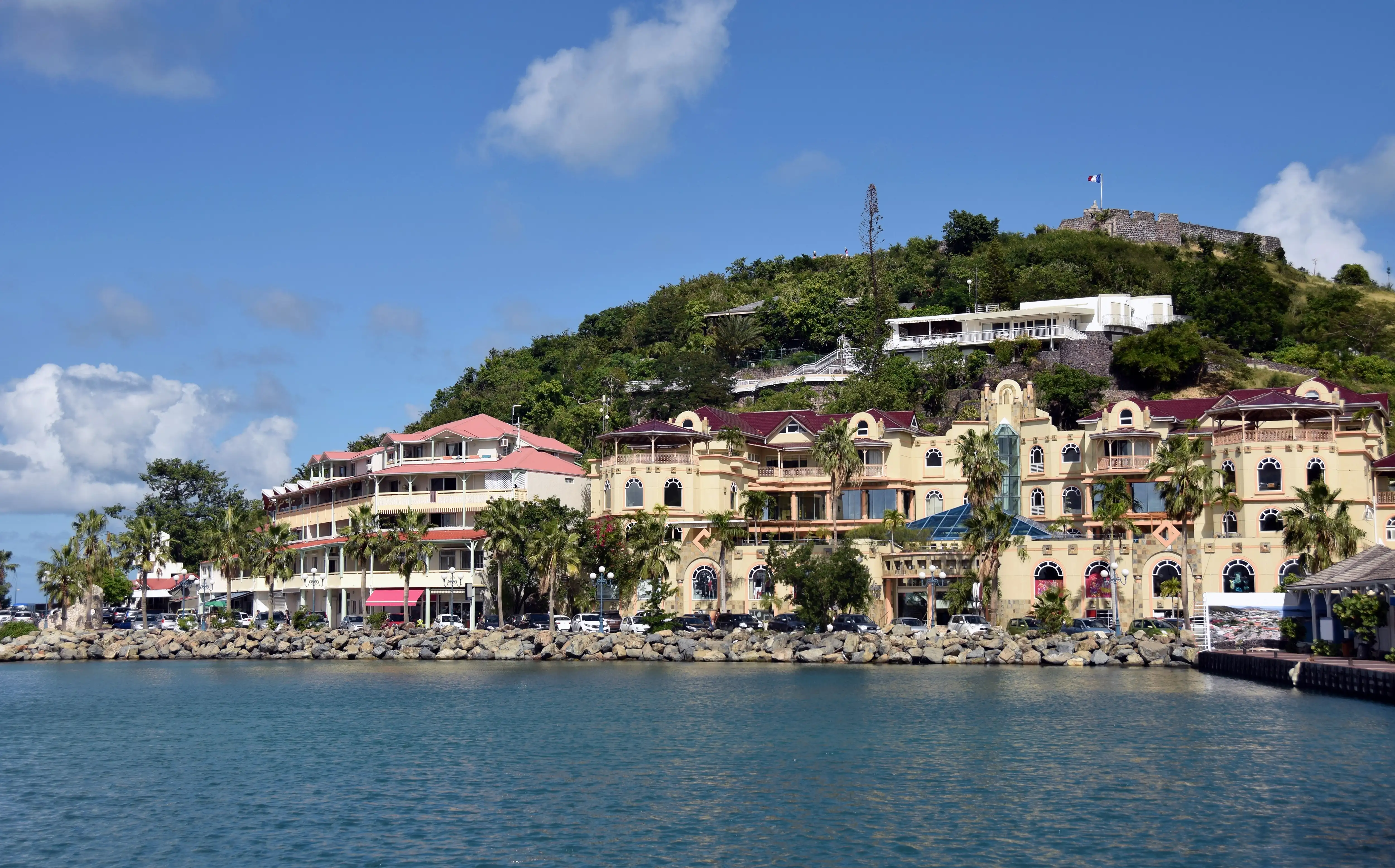 Row of yellow colonnaded waterfront buildings in Marigot with Fort Louis on the hill above