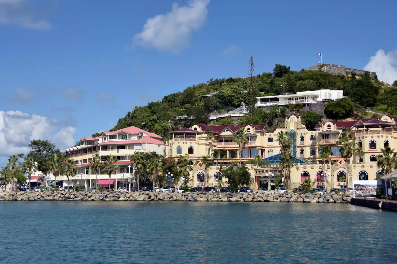 The waterfront promenade at Marigot, with palms along the walkway, moored boats in the bay, and the hills of the French side behind