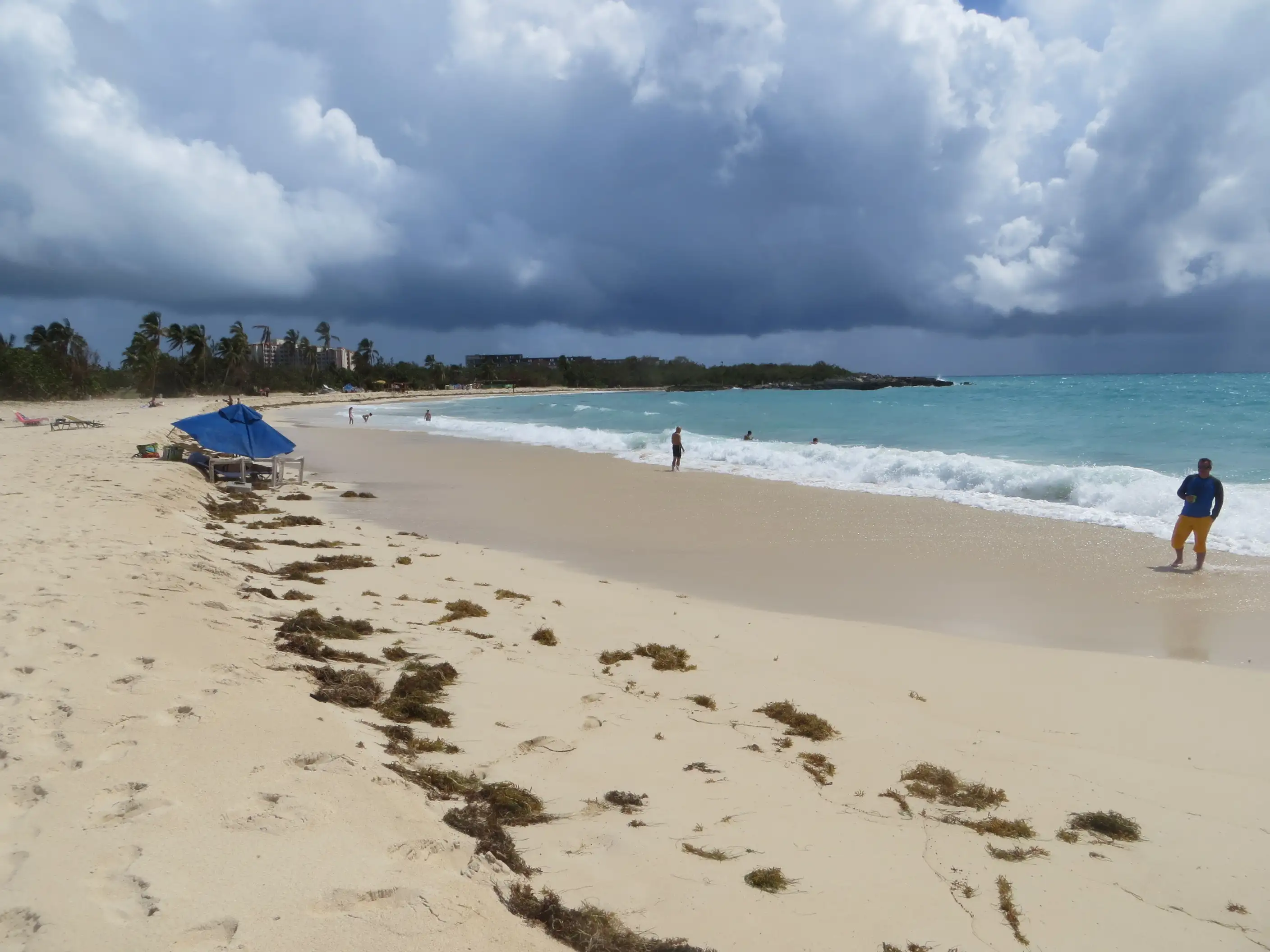 Empty shoreline at Mullet Bay Beach with a single beach umbrella and overcast sky, waves rolling in