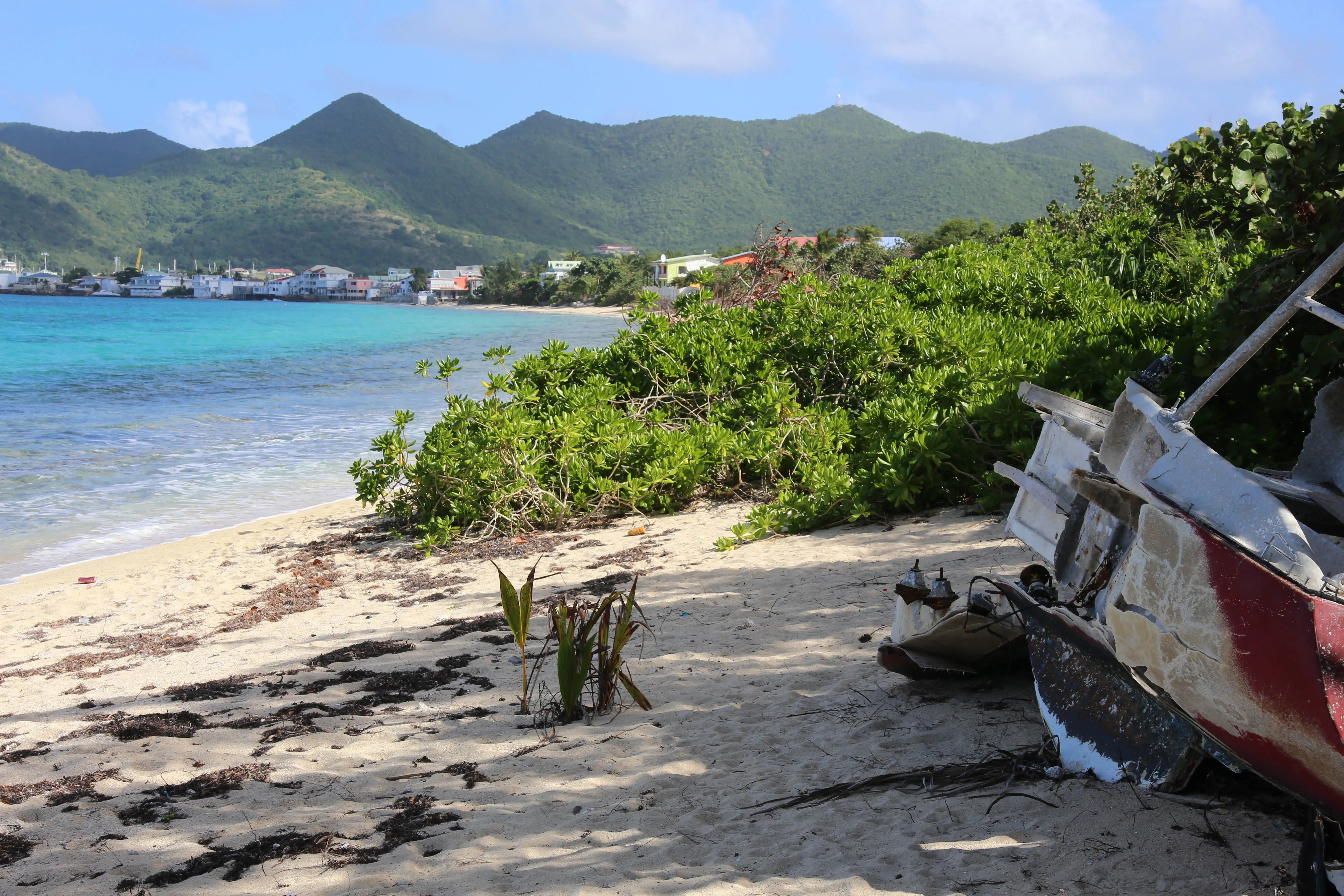 A small boat resting on the sand at the western end of Baie Nettlé, with the shoreline running away behind it