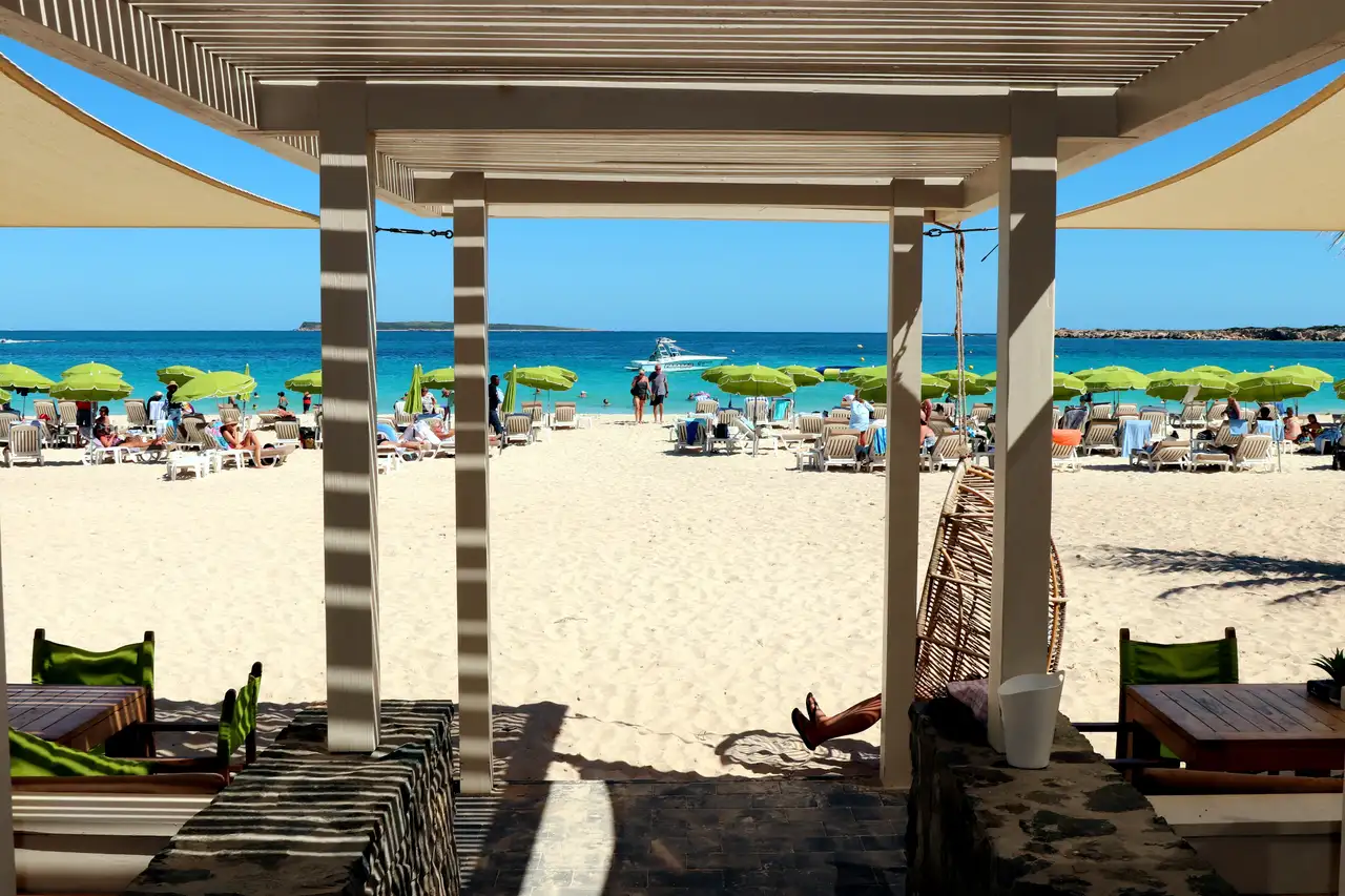 Rows of loungers under blue and white umbrellas on the white sand outside a beach bar at Orient Bay, with turquoise water beyond