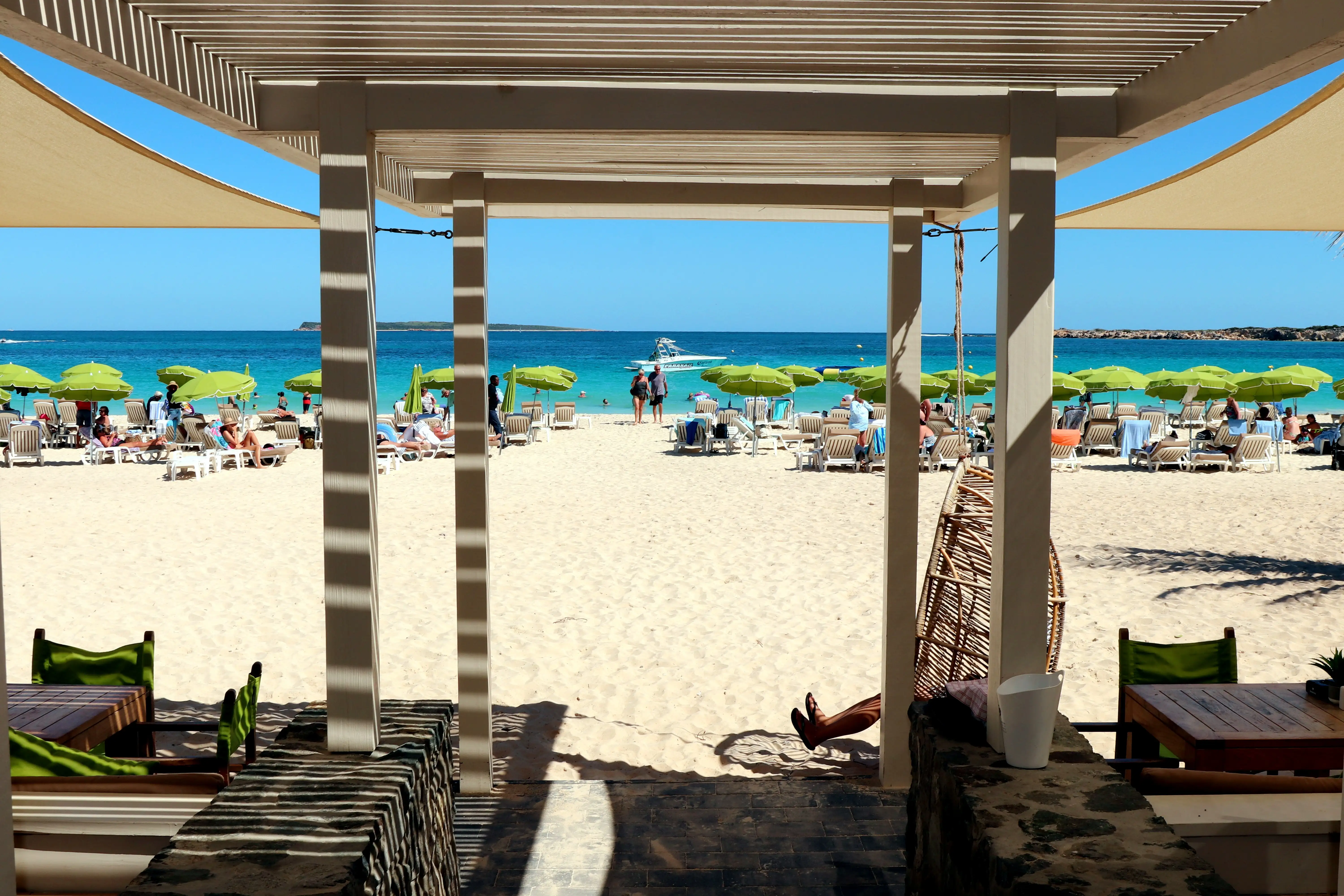 Rows of loungers under blue and white umbrellas on the white sand outside a beach bar at Orient Bay, with turquoise water beyond