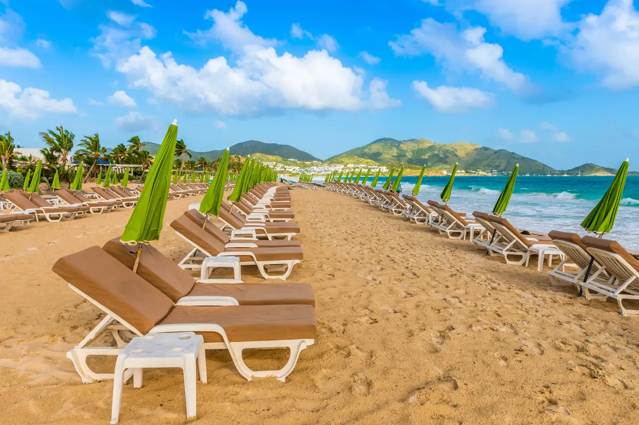 Long row of beach loungers and green umbrellas facing the ocean at Orient Bay