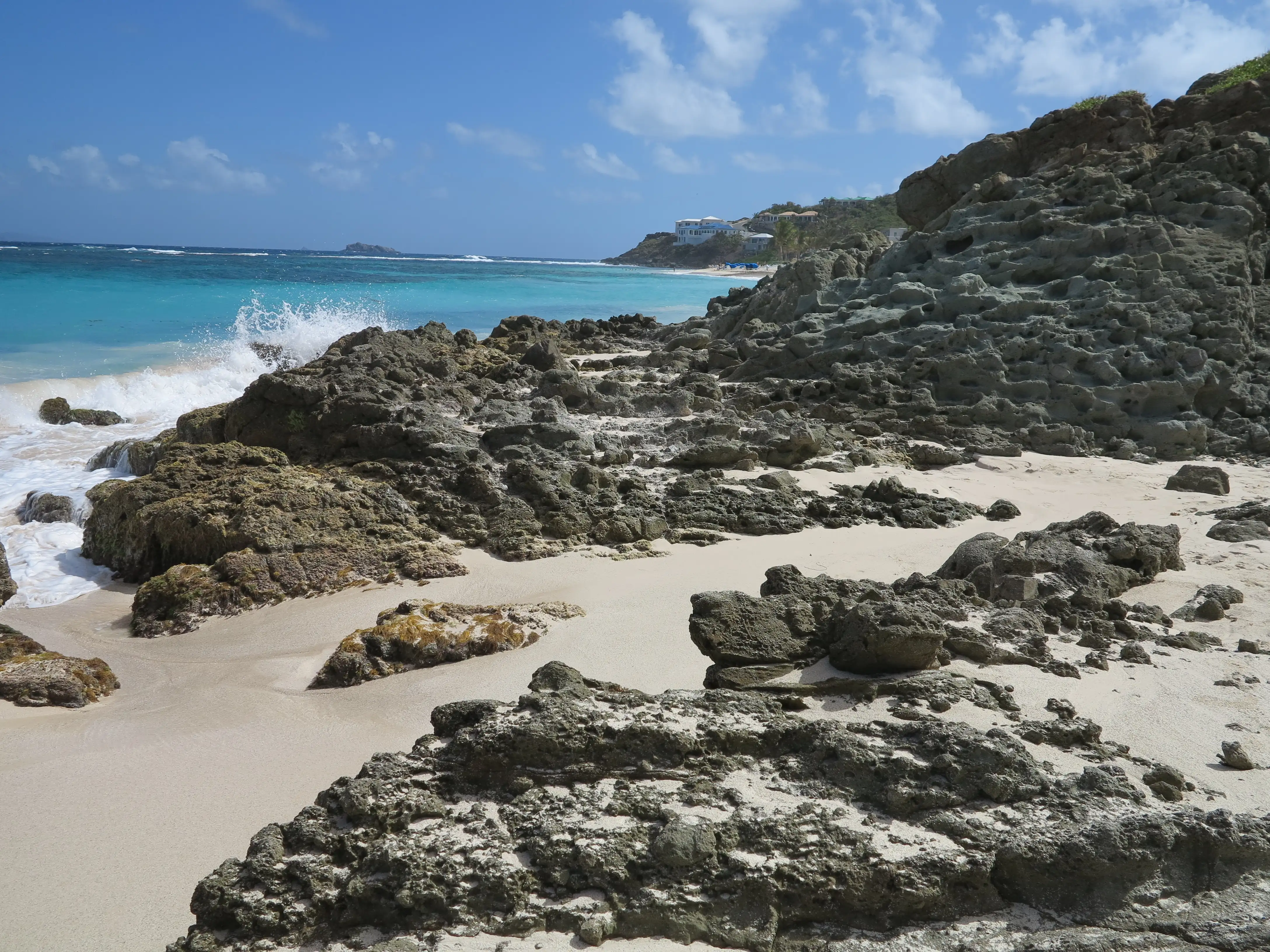 Atlantic waves breaking over rock and coral formations along Dawn Beach, the open-ocean shore adjoining Oyster Pond, under a blue sky