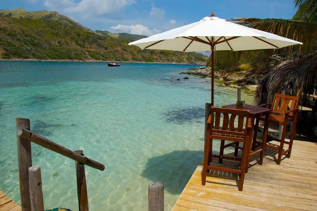 A beach bar with thatched umbrellas standing beside a wooden pier on a small Caribbean island