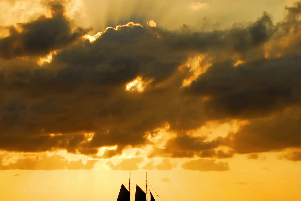 Silhouette of a sailboat against a dramatic golden sunset sky over open water