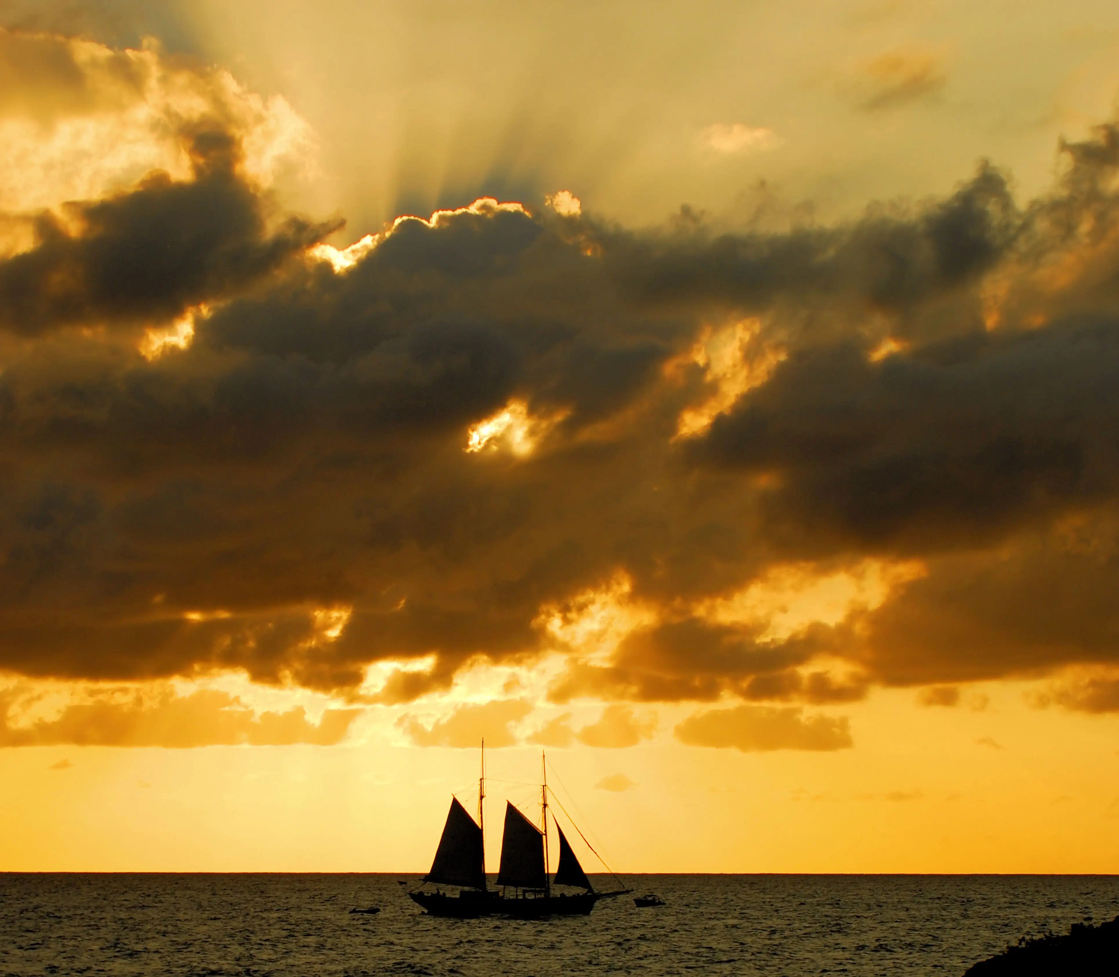 Silhouette of a sailboat against a dramatic golden sunset sky over open water