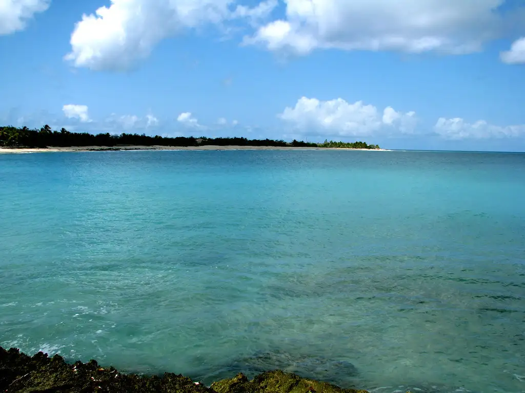 Empty pale sand curving between low green headlands at Baie aux Prunes, with clear turquoise water and nobody on the beach