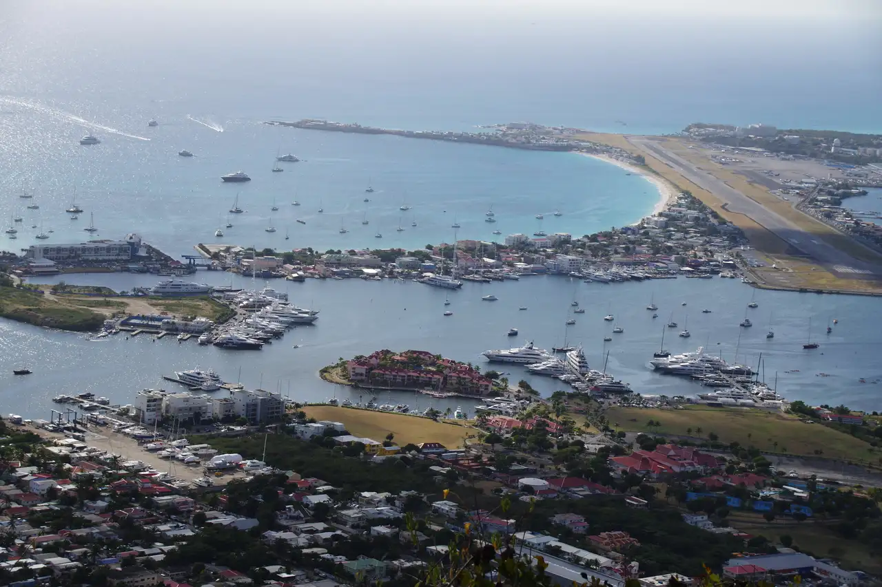 Elevated view over Simpson Bay and the lagoon from a hilltop, showing the long curve of the beach between the headland and the airport