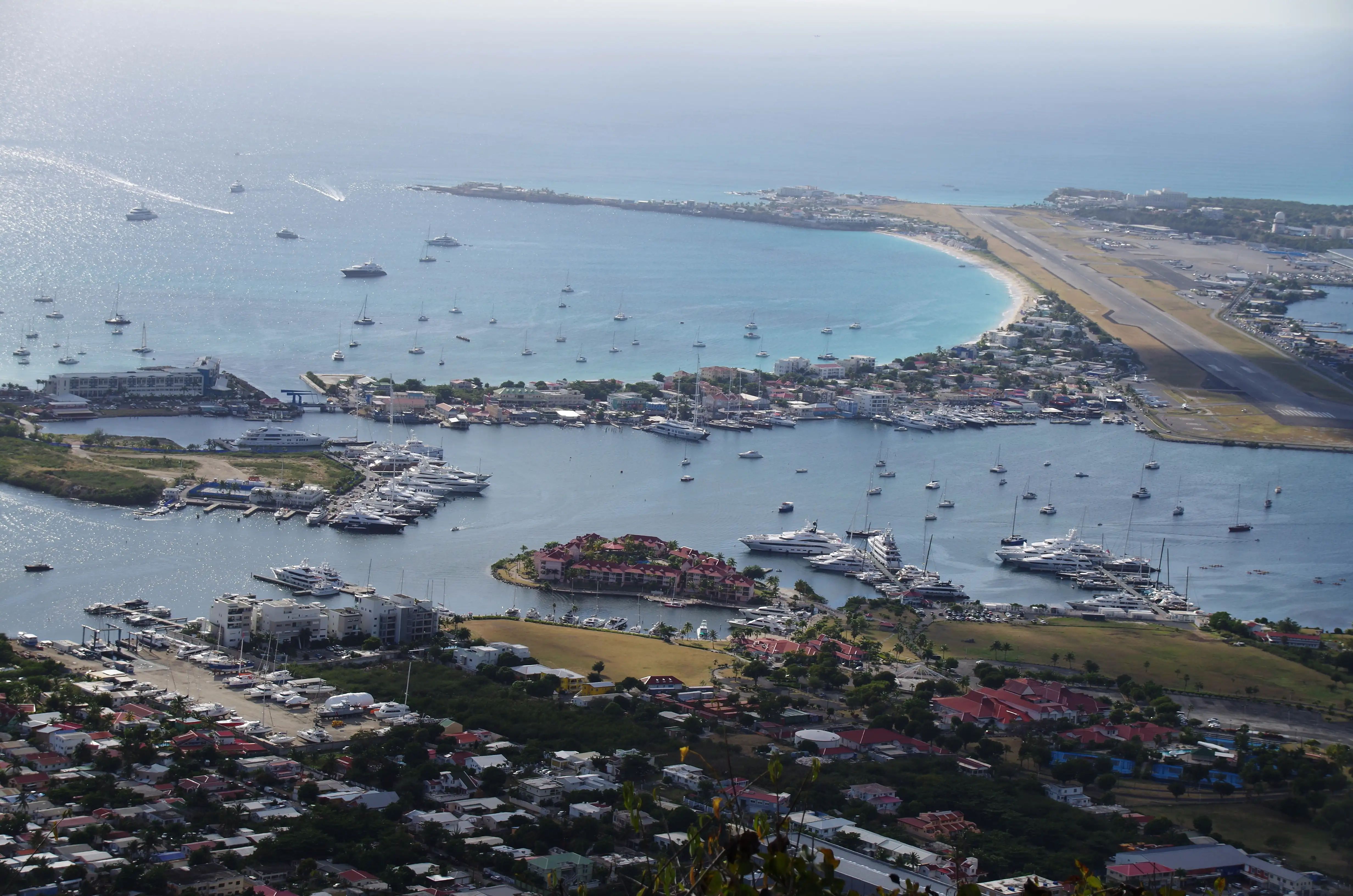 Elevated view over Simpson Bay and the lagoon from a hilltop, showing the long curve of the beach between the headland and the airport