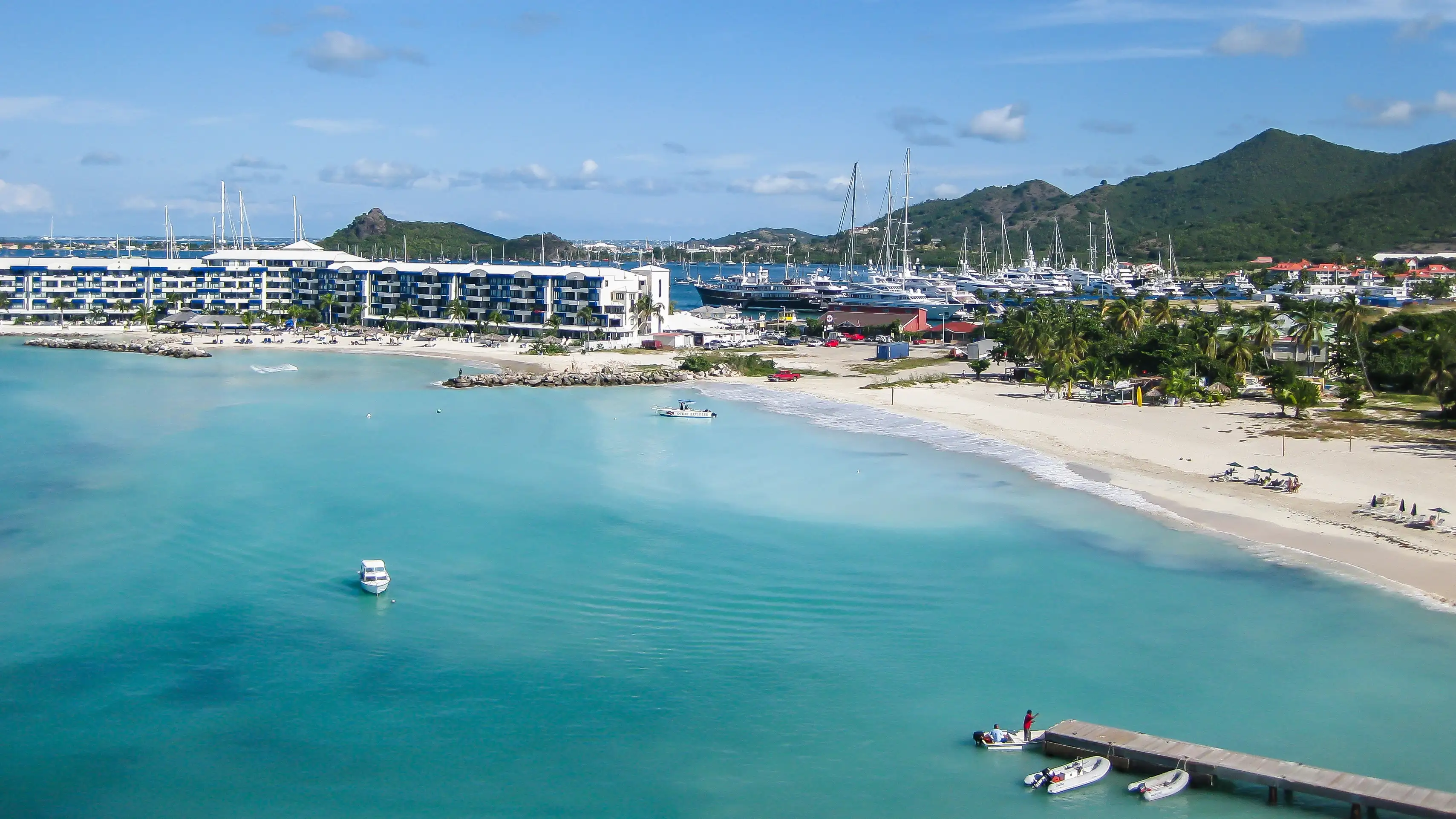 Aerial view of Simpson Bay beach with a row of condo and resort buildings and a marina full of yachts