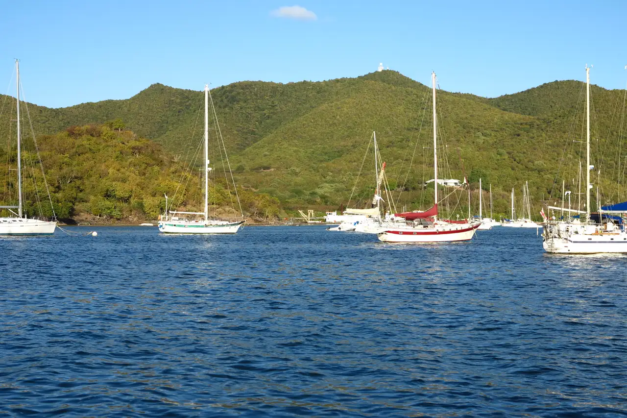 Sailboats and yachts anchored in Simpson Bay lagoon with a green hillside backdrop under blue sky