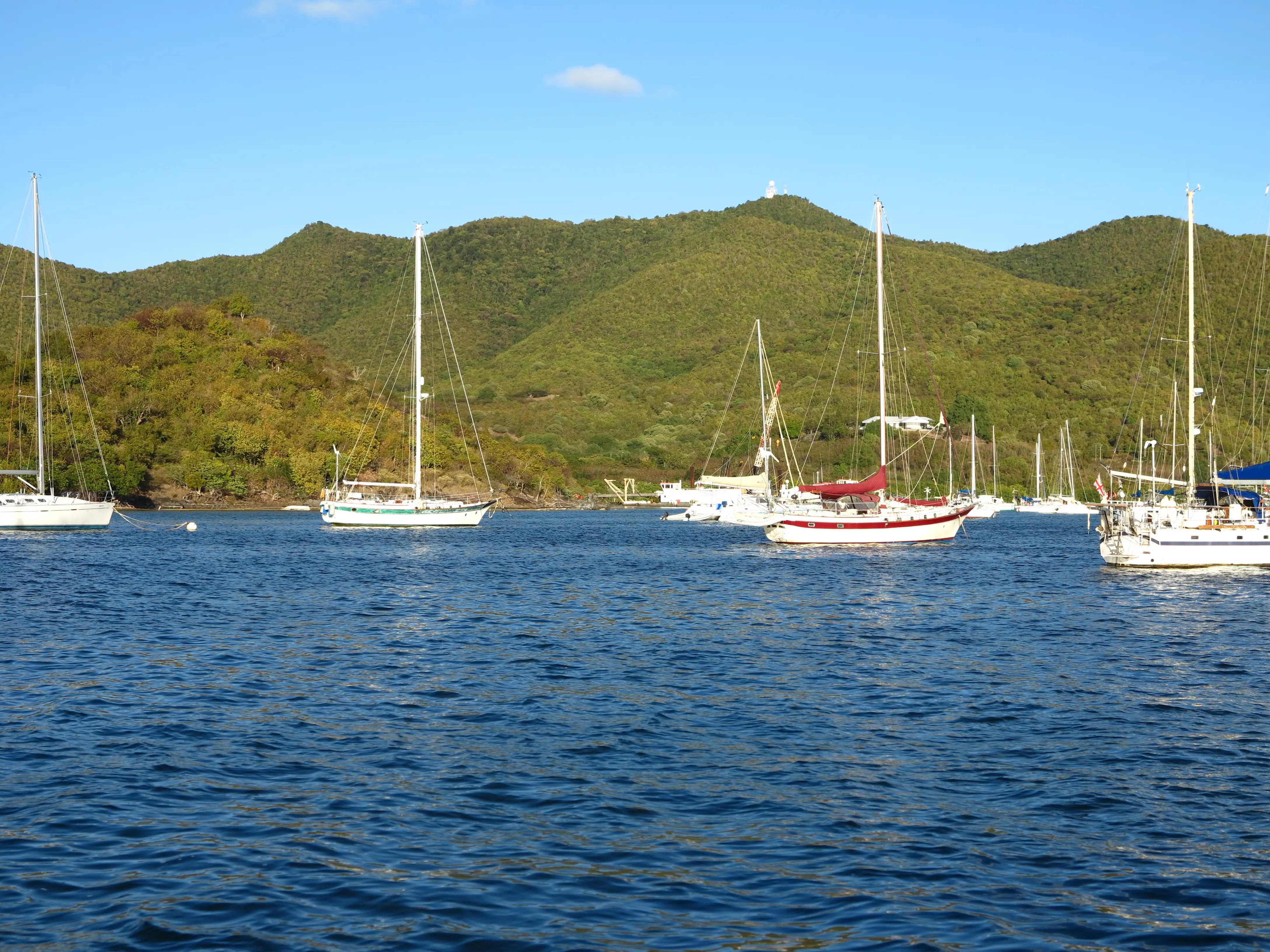 Sailboats and yachts anchored in Simpson Bay lagoon with a green hillside backdrop under blue sky